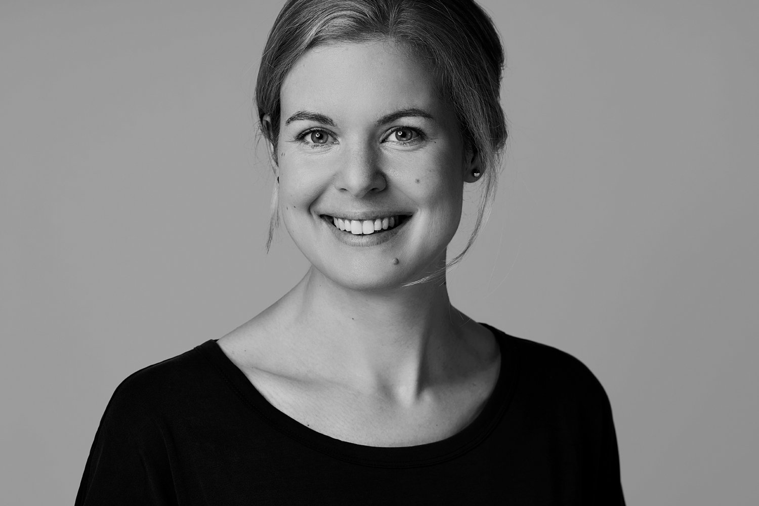 Ein schwarz-weiß Bewerbungsfoto von einer blonden Frau, die in die Kamera lächelt