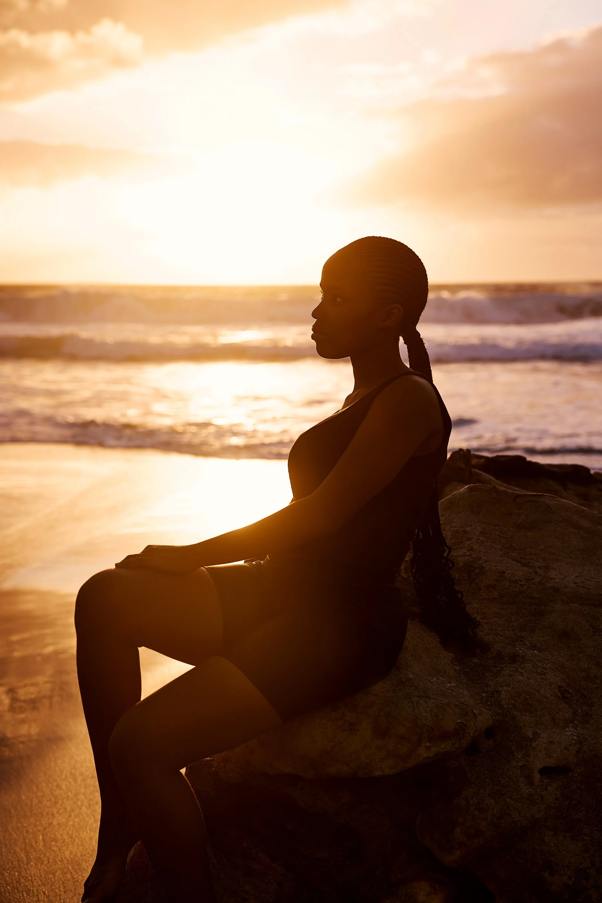 Eine junge Frau sitzt im Gegenlicht auf einem Felsen am Meer