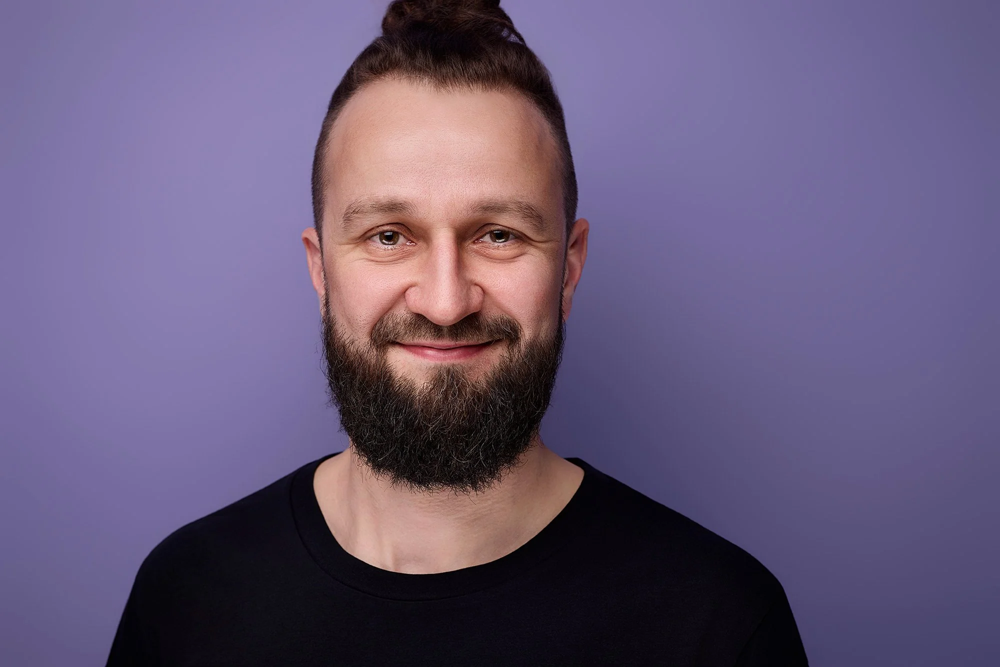 Ein Porträt von einem Mann mit Bart vor einem fliederfarbenen Hintergrund