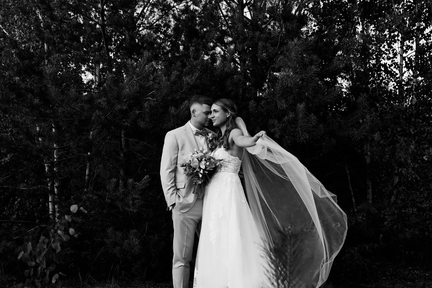 Ein schwarz-weiß Bild von einem Brautpaar, was vor einem Wald steht