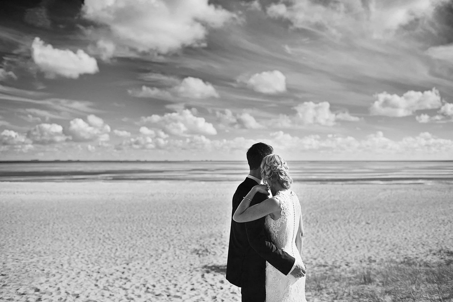 Ein Hochzeit Pärchen schaut am Strand verliebt in den Wolkenhimmel