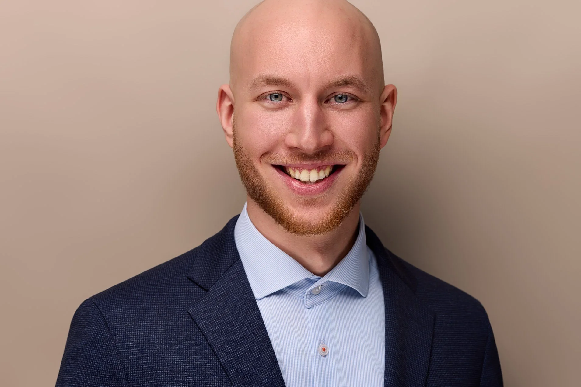 Ein Mann mit Bart lächelt vor einem erdfarbenen Hintergrund in die Kamara des Fotografen