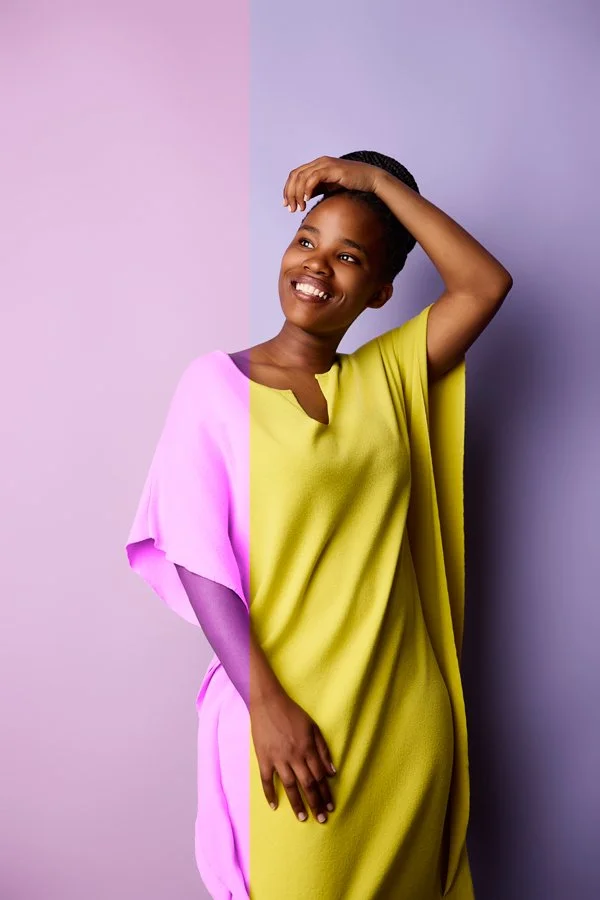 Eine junge Frau im gelben Kleid posiert für den Portrait Fotografen vor einer fliederfahrenden Wand