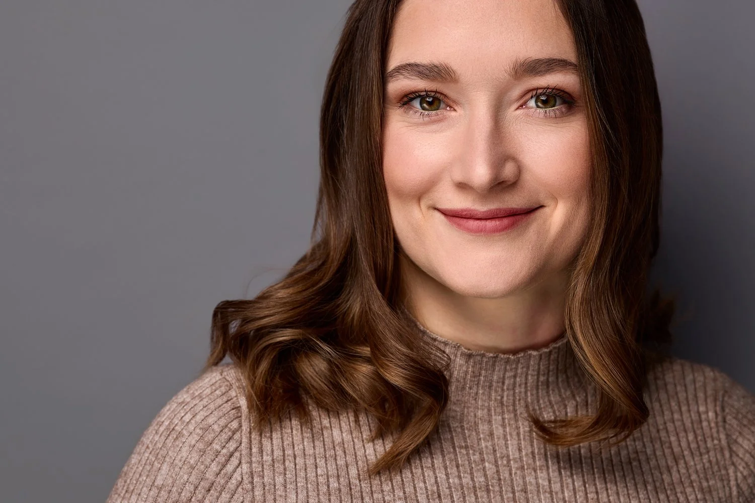 Ein Business Portrait von einer Frau mit blonden Haaren, die in die Kamera lächelt und vor einem grauen Hintergrund steht