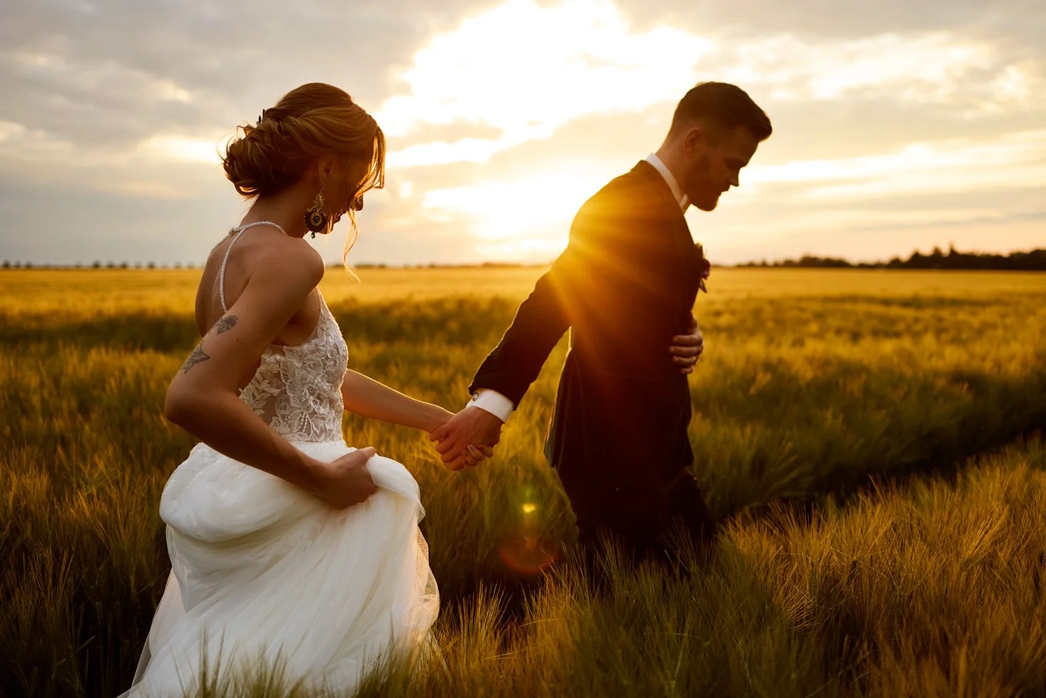Ein Brautpaar läuft bei Sonnenuntergang über ein Feld