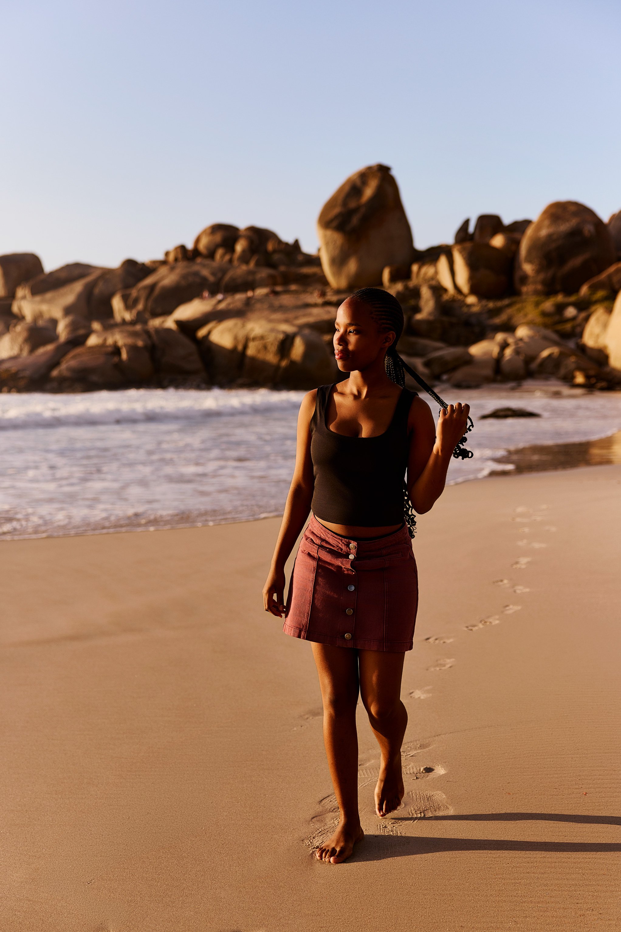 Eine junge Frau spaziert am Strand entlang bei Sonnenuntergang