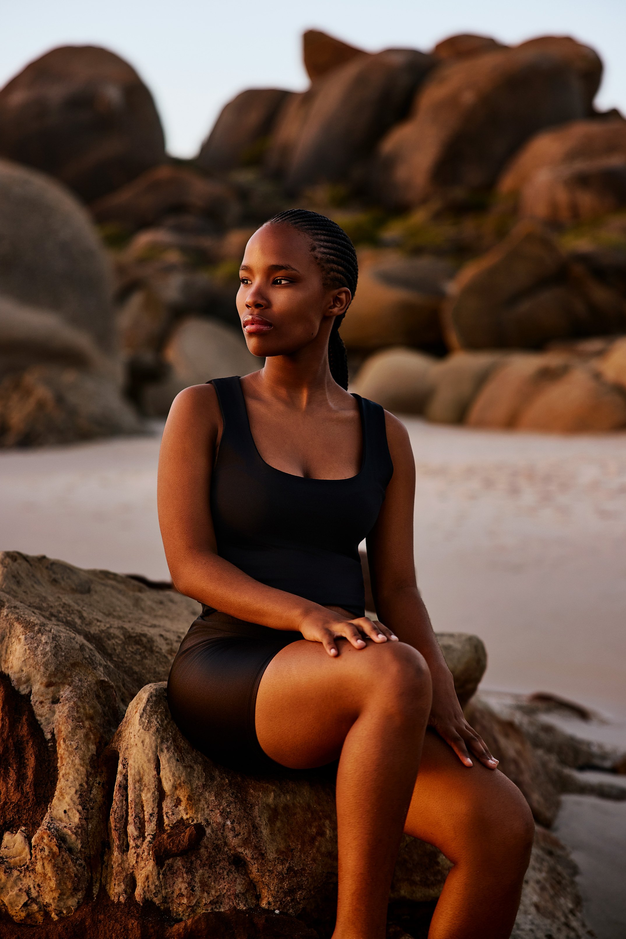 Eine Frau sitzt am Strand auf einem Felsen im Abendsonnenlicht