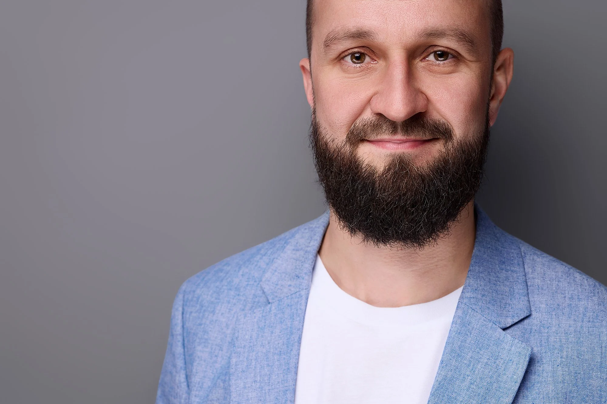 Mann mit Bart und blauem Jacket vor einem grauem Hintergrund