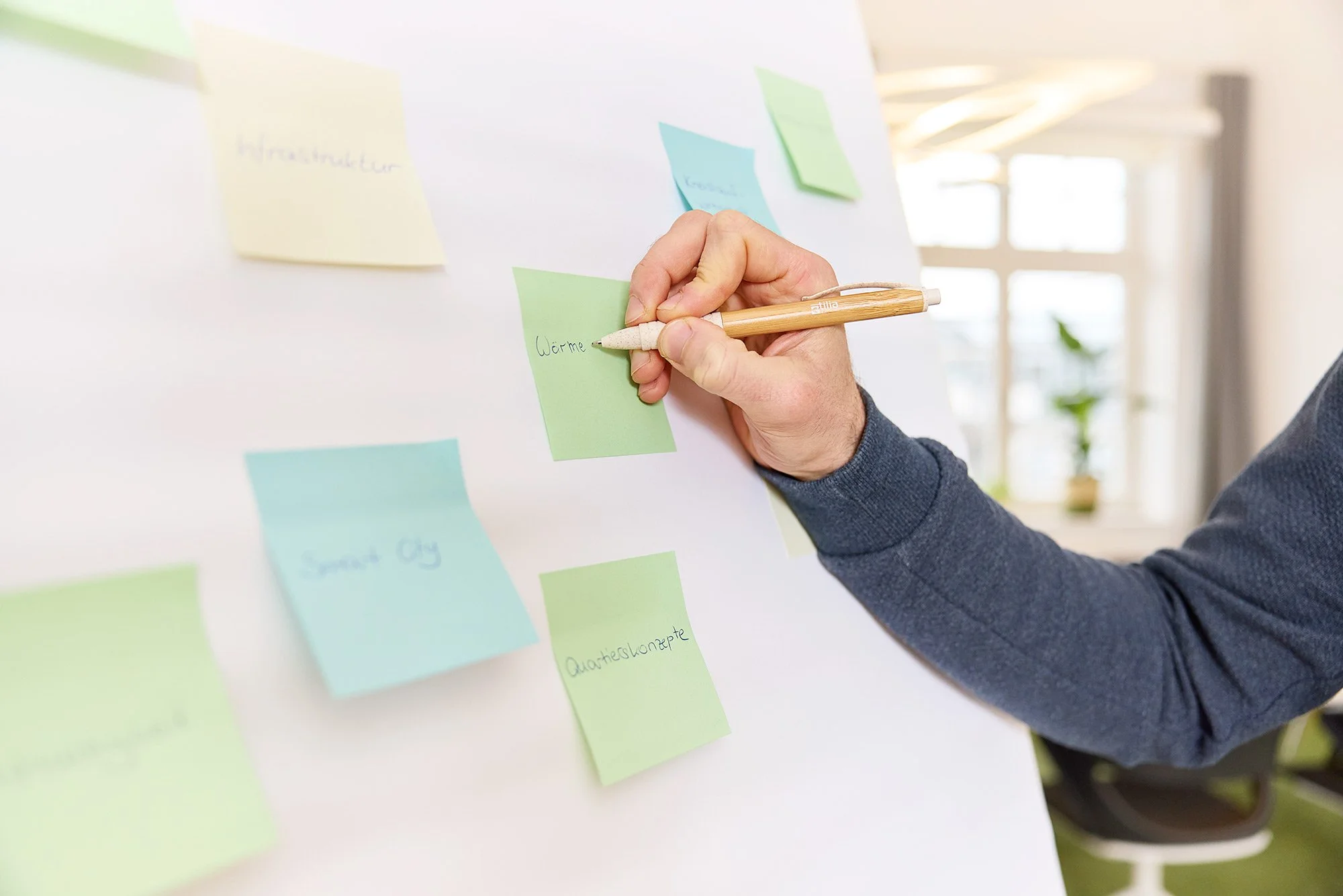 Ein Detail von einem Mann, der mit einem Kugelschreiber einem Post-It beschreibt