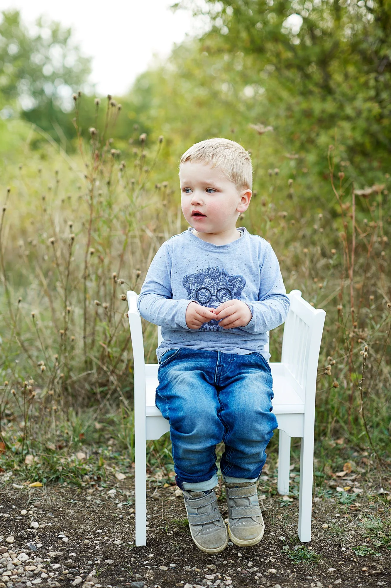 Ein kleiner junge sitzt auf einem weißen Stuhl im Grünen bei einem Familienfotoshooting