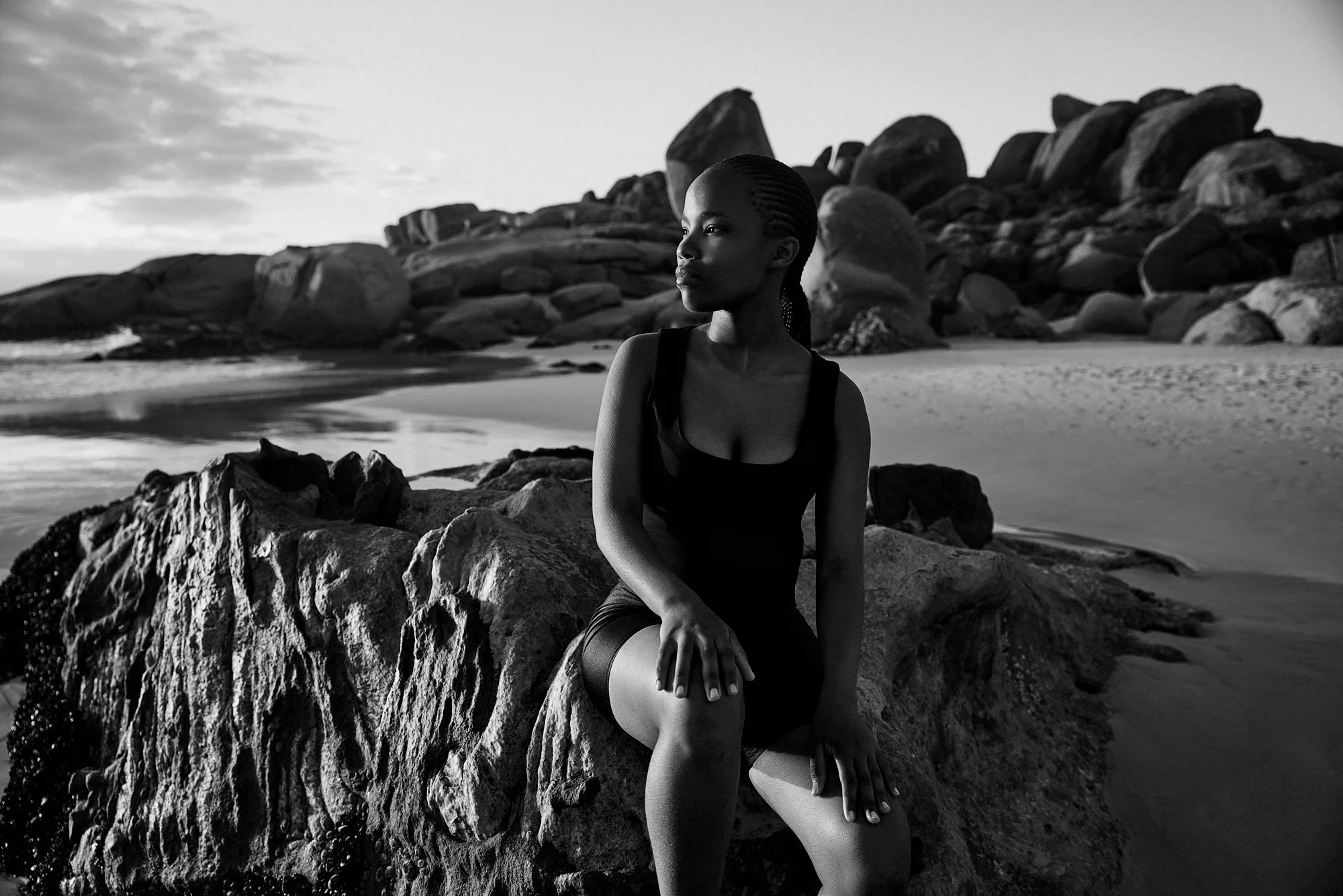 Ein Portraitfoto von einer jungen Frau, die auf einem Felsen am Strand sitzt