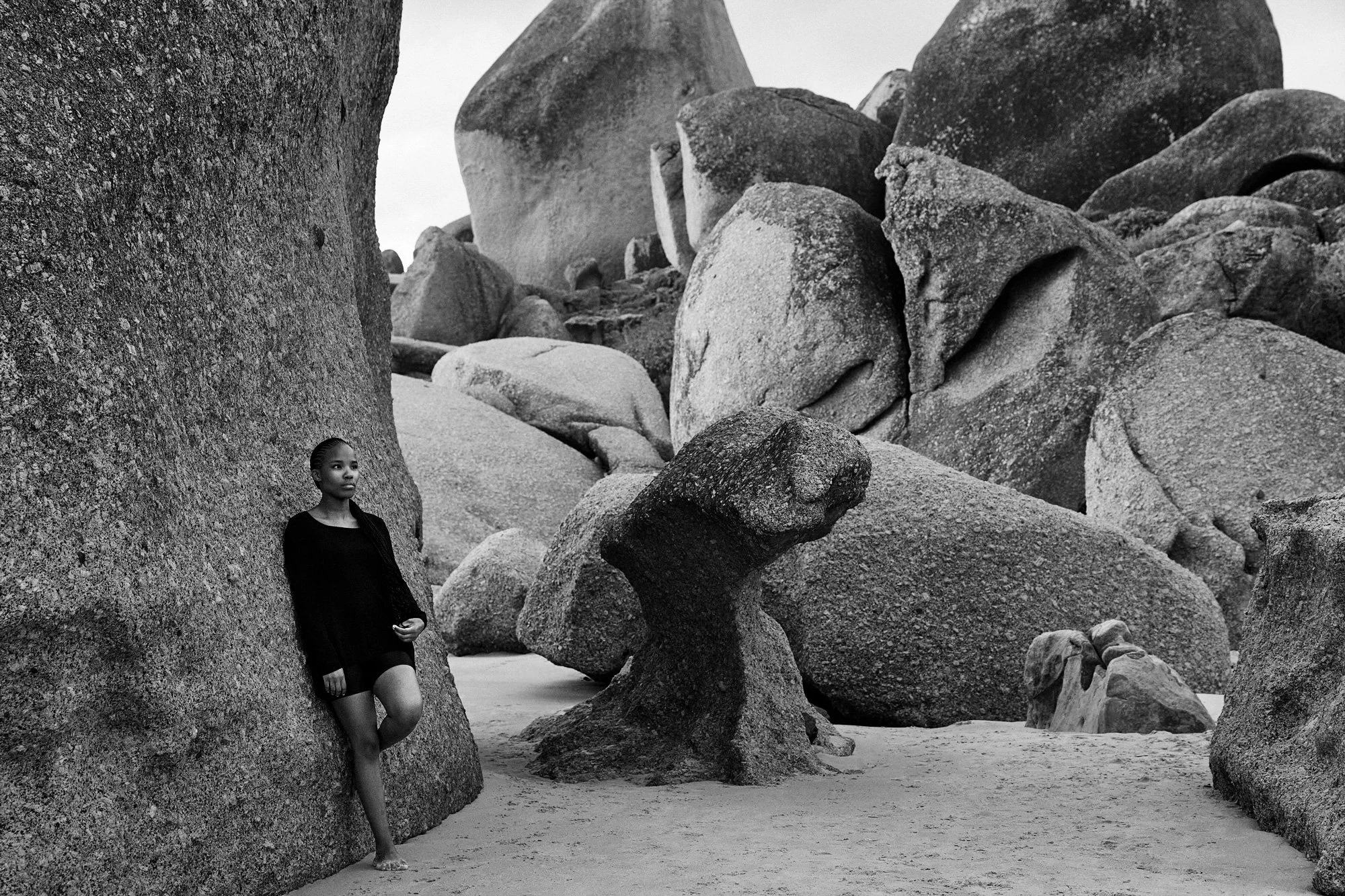 Eine Schwarz gekleidete Frau lehnt an einem großen Felsen