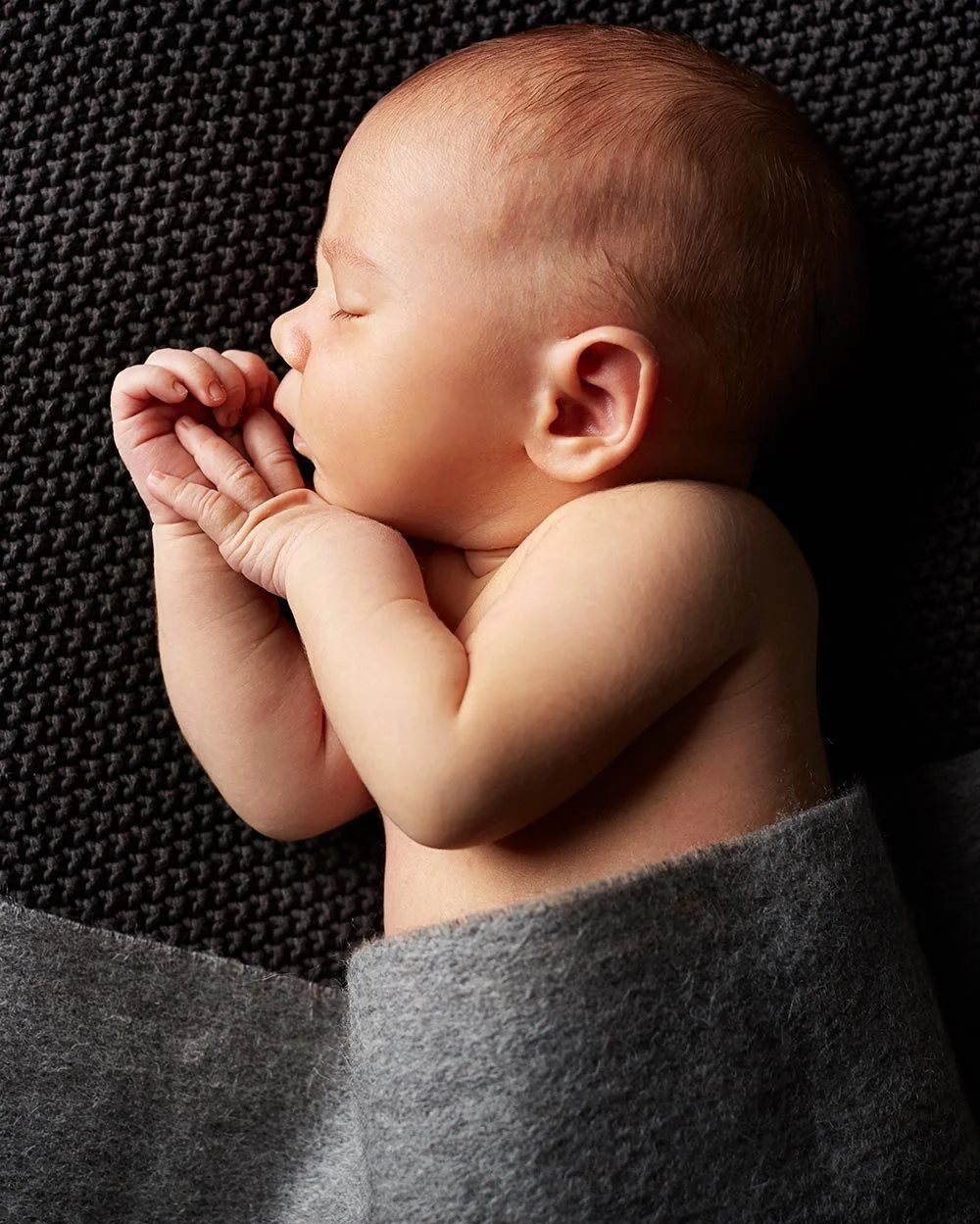 Ein Baby liegt auf einer schwarzen Decke und schläft
