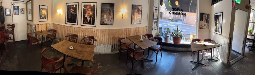 Inomhusinterior av ett café eller restaurang med trämöbler, väggfoton och stora fönster med utsikt utomhus.