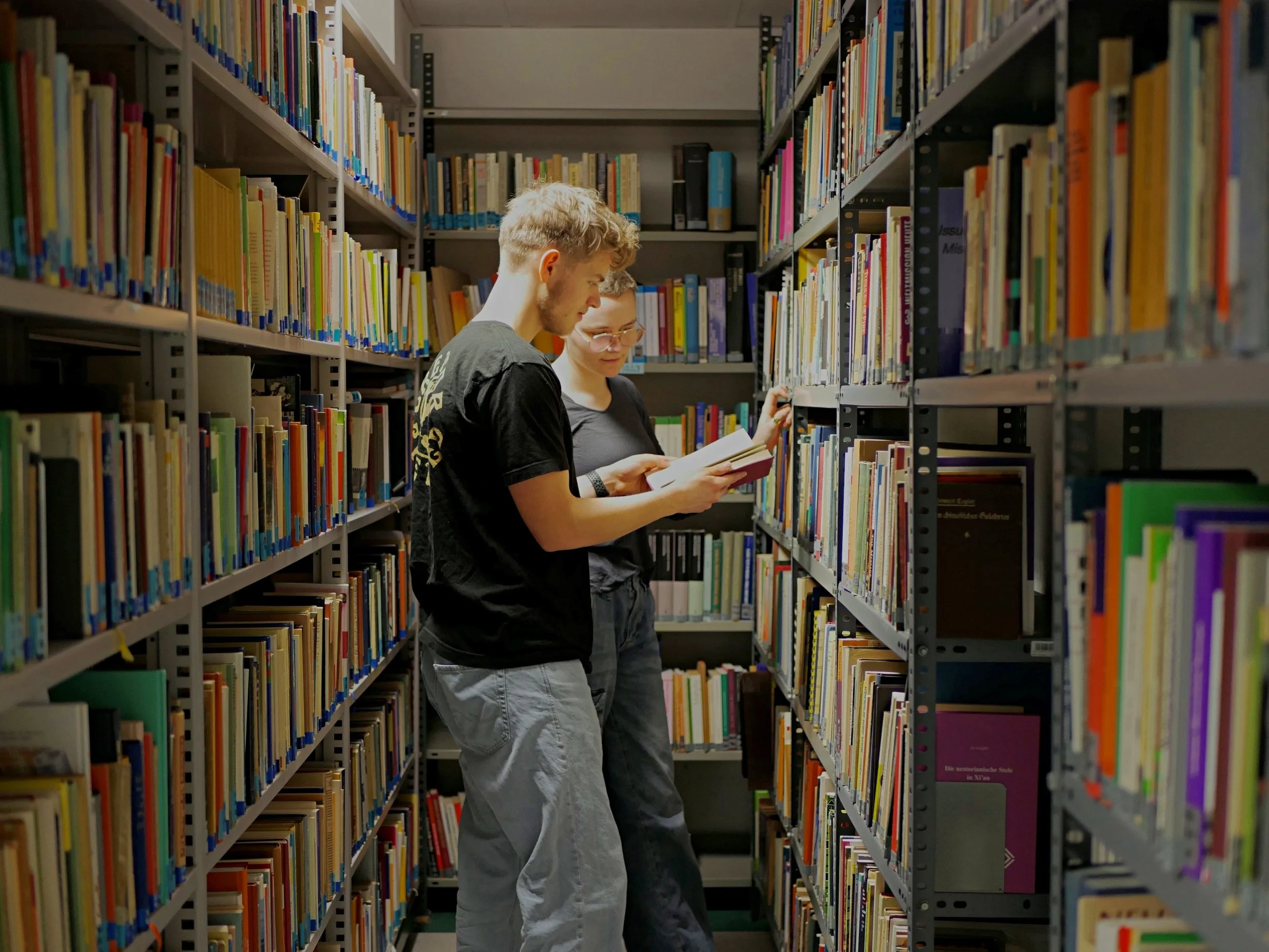 Zwei Studierende zwischen zwei Regalen voller Bücher