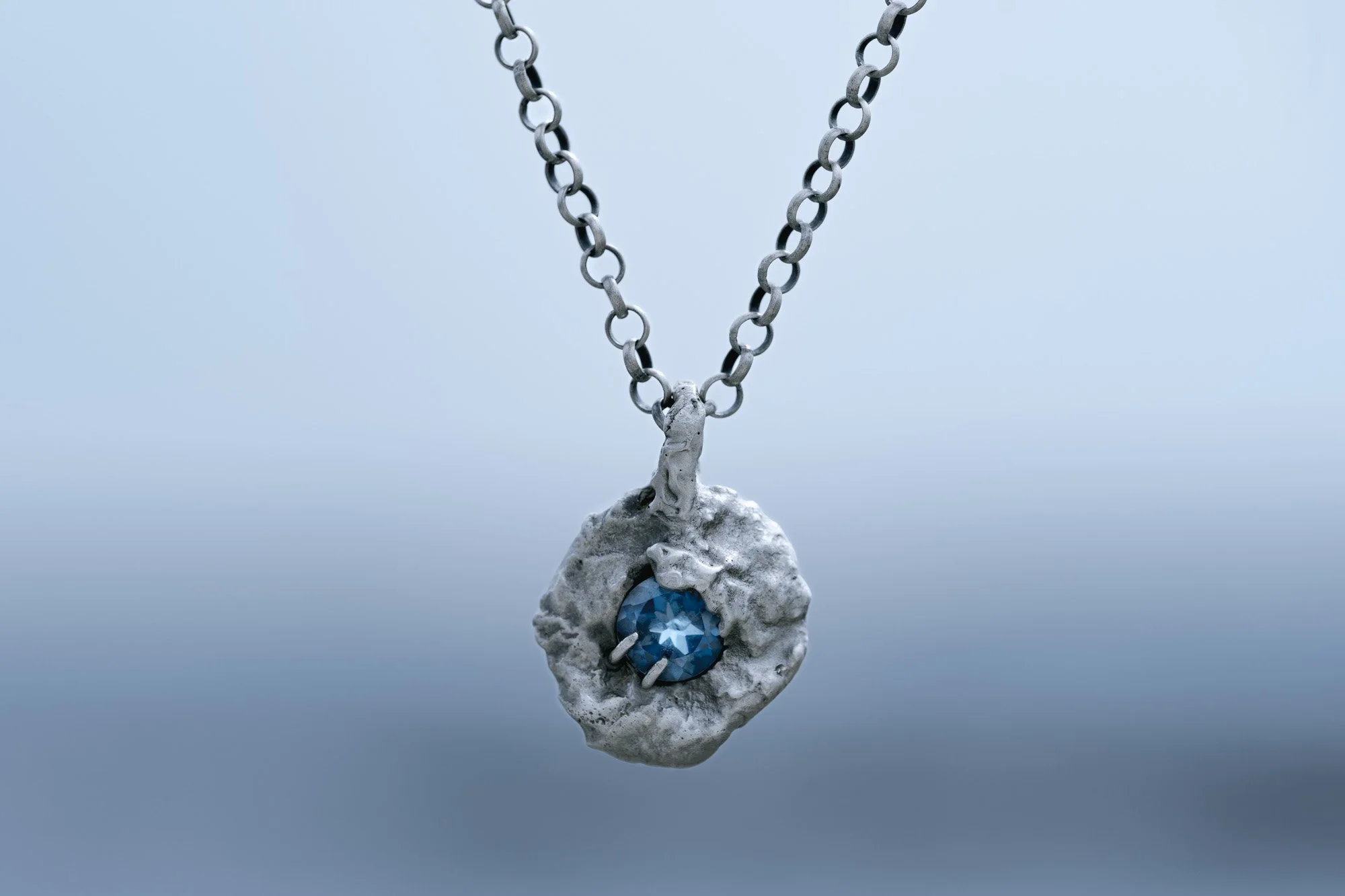 colgante de plata con piedra topacio London Blue sobre fondo azul degradado