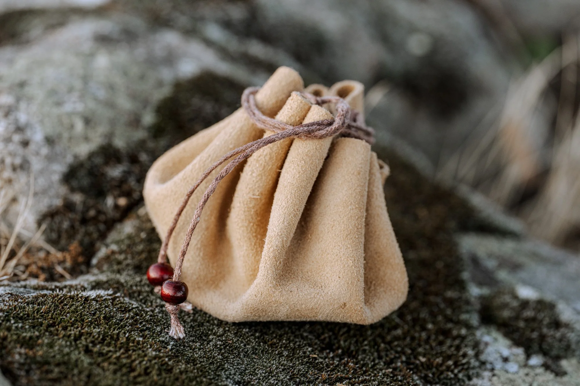 Bolsa de tela beige sobre una superficie de roca con un cordón marrón y cuentas de madera.