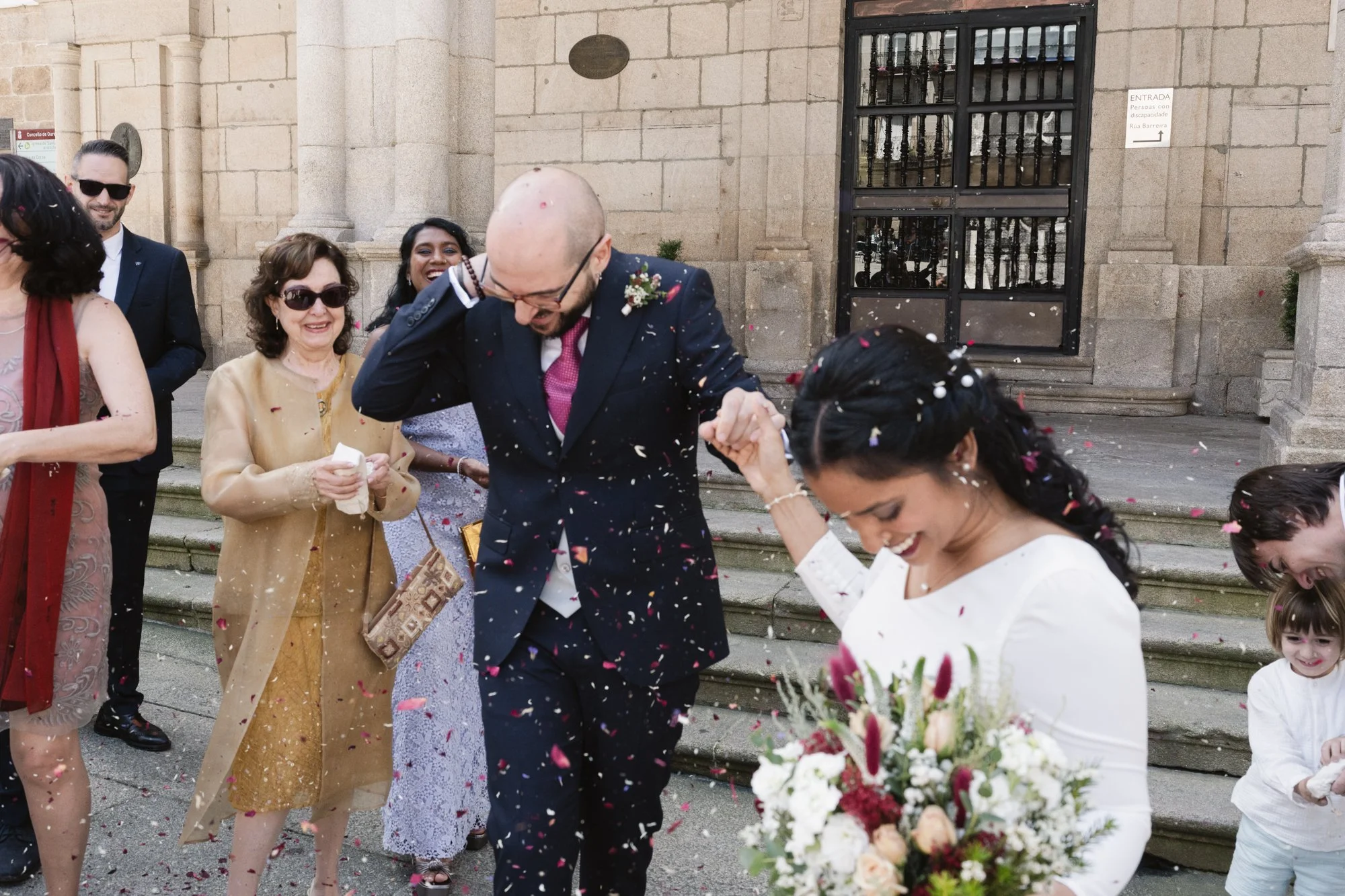 Pareja de recién casados a la del ayuntamiento, rodeados por toda su familia que lanza arroz y pétalos