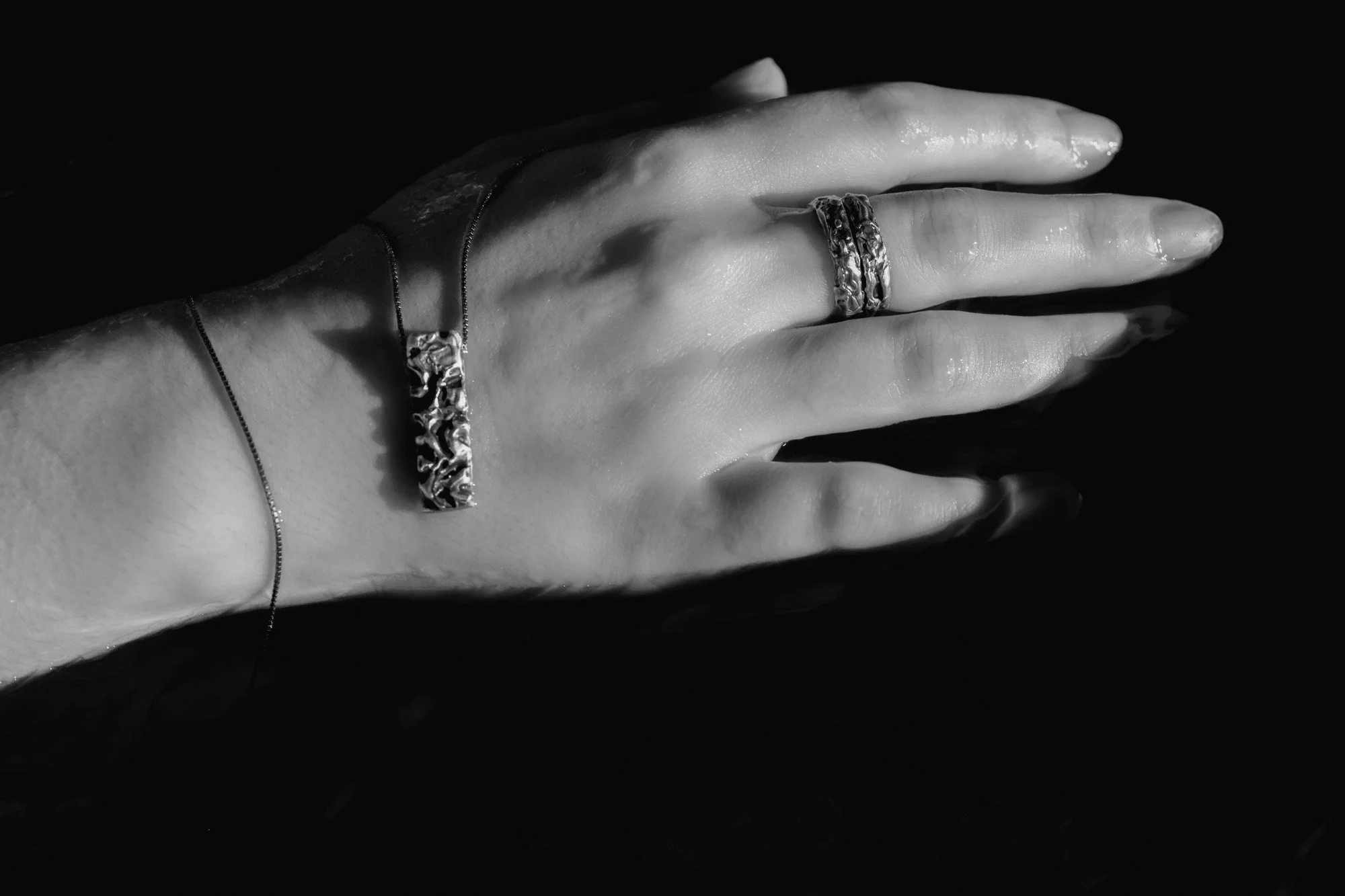 mano con anillos y colgante de plata sobre el agua, jugando con las sombras