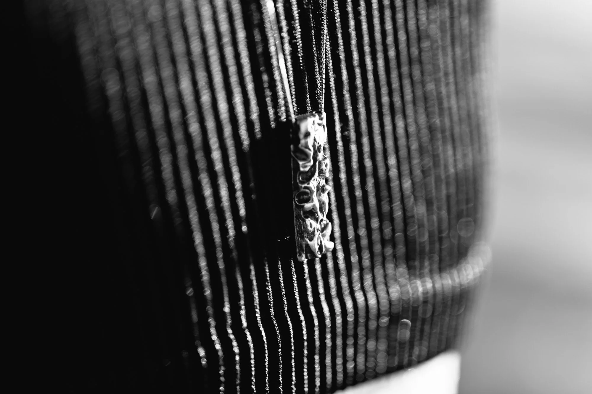Textura de tela negra con líneas verticales y un aplique metálico en primer plano.