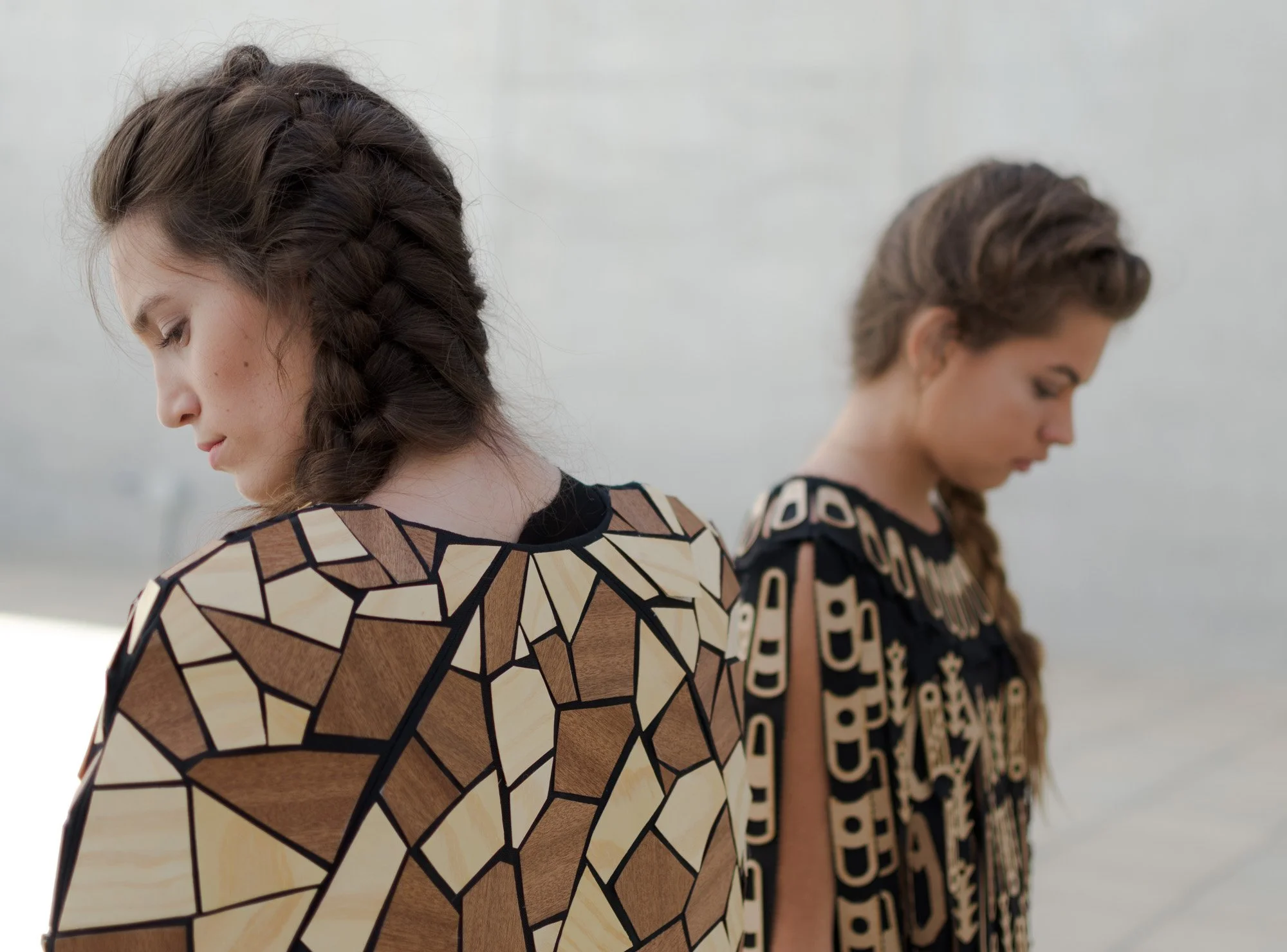 Dos mujeres con trenzas, usando prendas con diseños geométricos en tonos marrones y beige, en un entorno al aire libre.