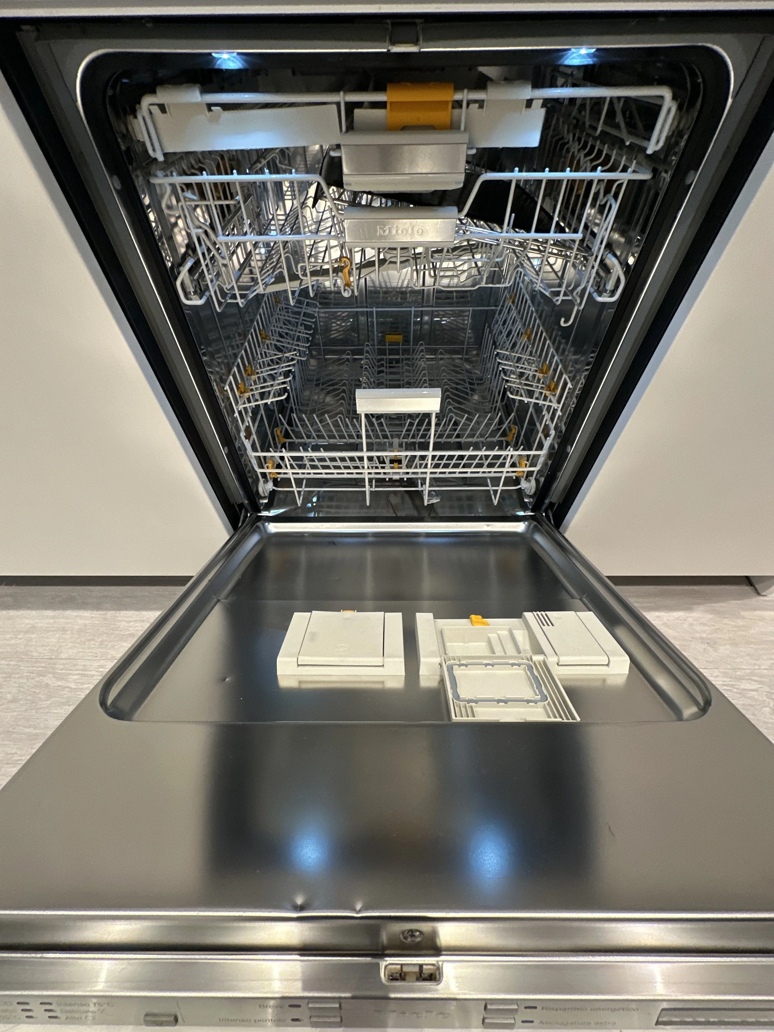 Empty modern stainless steel dishwasher with open door, showing racks and compartments inside.