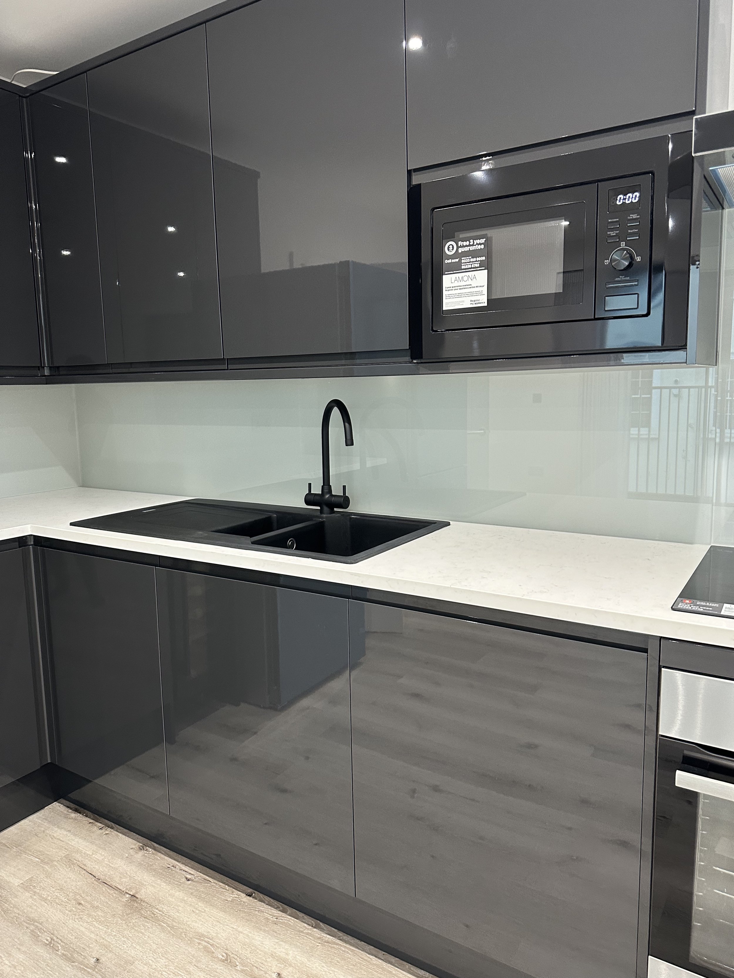 Modern kitchen with dark gray cabinets, white countertop, black sink, and built-in microwave oven.