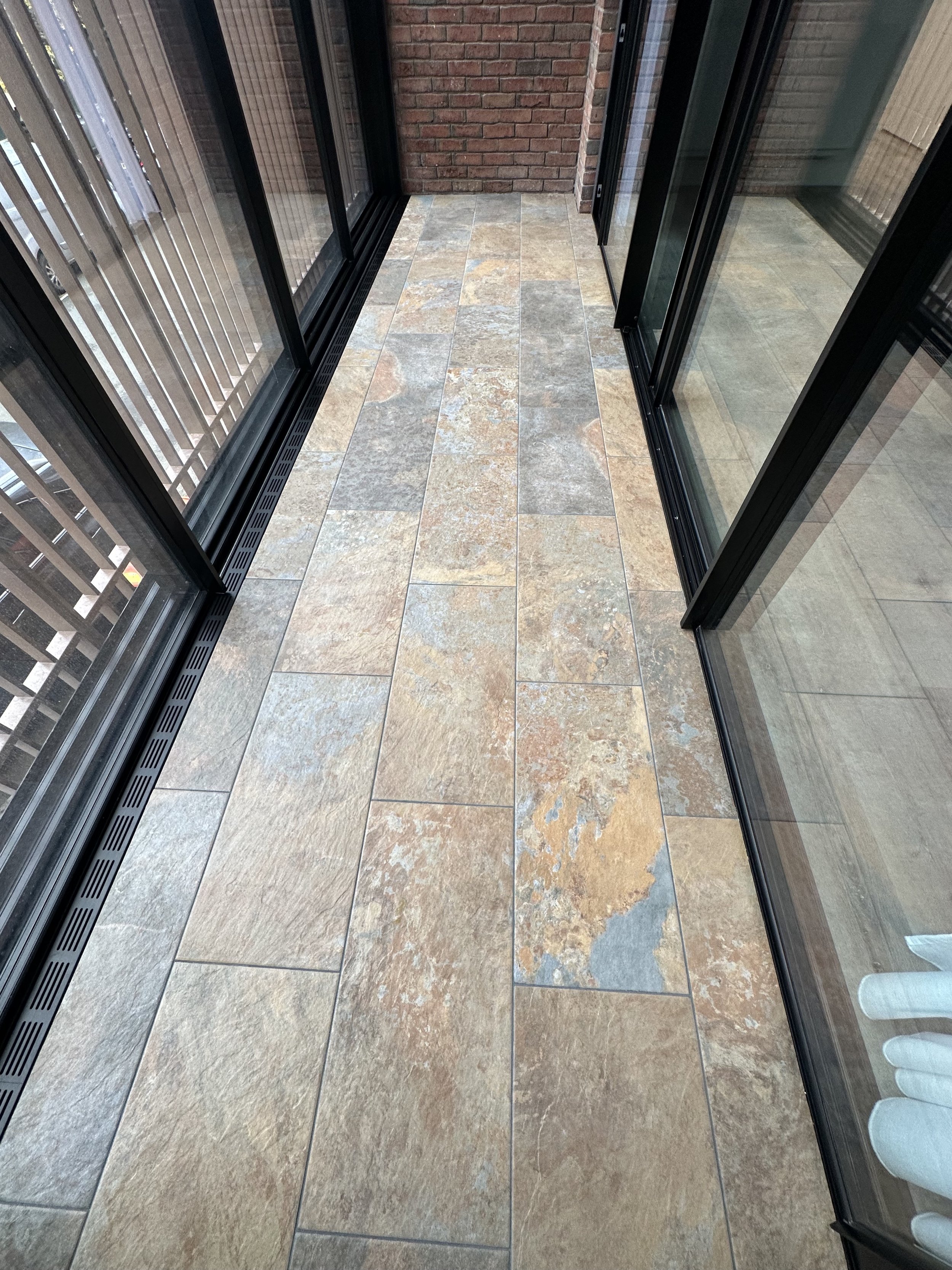 Balcony with tiled floor, glass sliding doors, metal railing, brick wall, and a window.