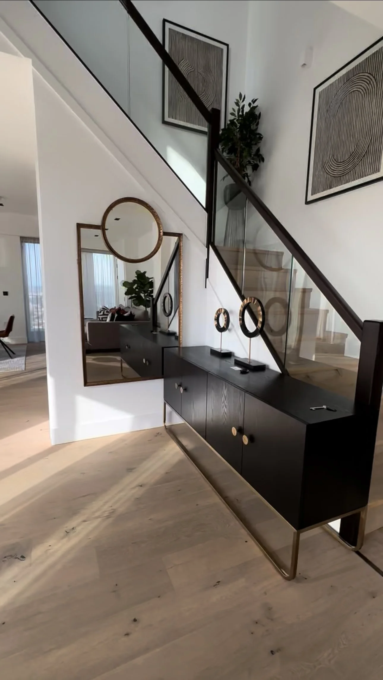 Modern living room with a staircase, black sideboard, round decorative objects, and artwork with geometric patterns on the wall.