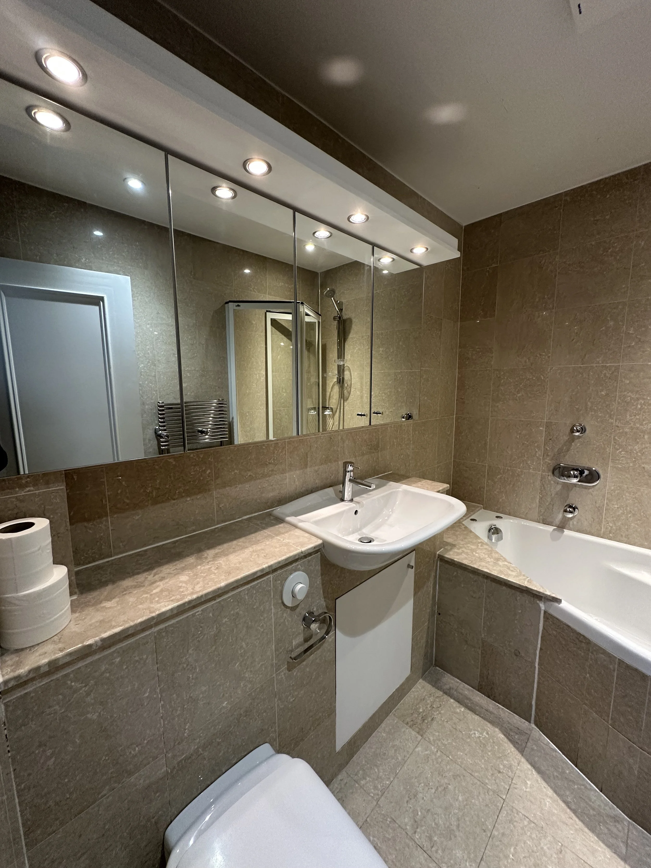A bathroom with a large mirror, lights, a sink, a bathtub, and a shower.
