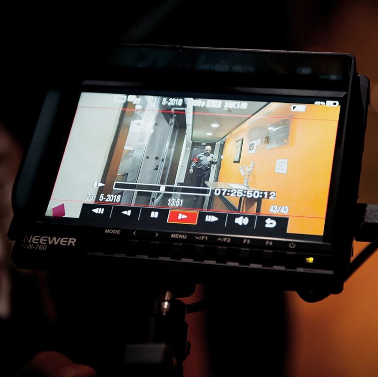 Video camera screen showing a man walking down a hallway with orange walls and a table with a decorative piece on it.