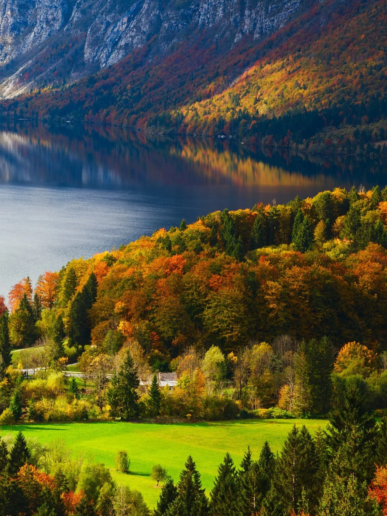 Scenic view of a lake surrounded by colorful autumn trees, with hills and mountains in the background.