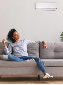 Woman relaxing on a gray sofa in a modern living room with a white wall and air conditioner unit