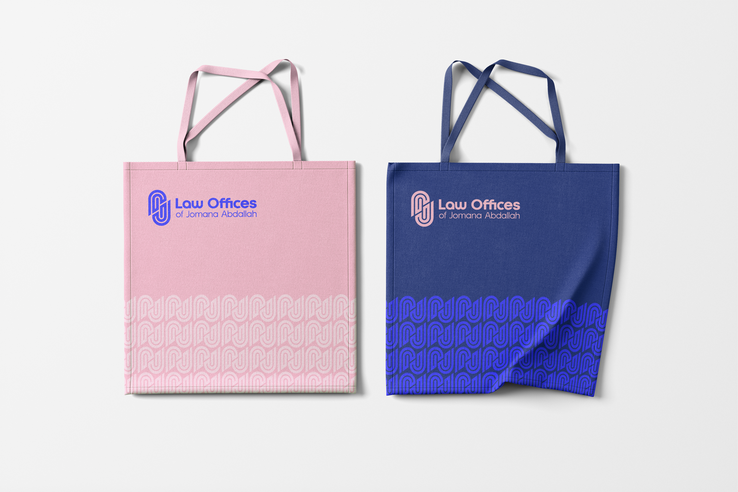 Two tote bags, one pink and one blue, with matching handles and the logo of Law Offices of Jomana Abdallah printed on the upper left. The pink bag has blue logo and text, with a pattern of interconnected lines at the bottom. The blue bag has pink logo and text, with a pattern of interconnected lines at the bottom.