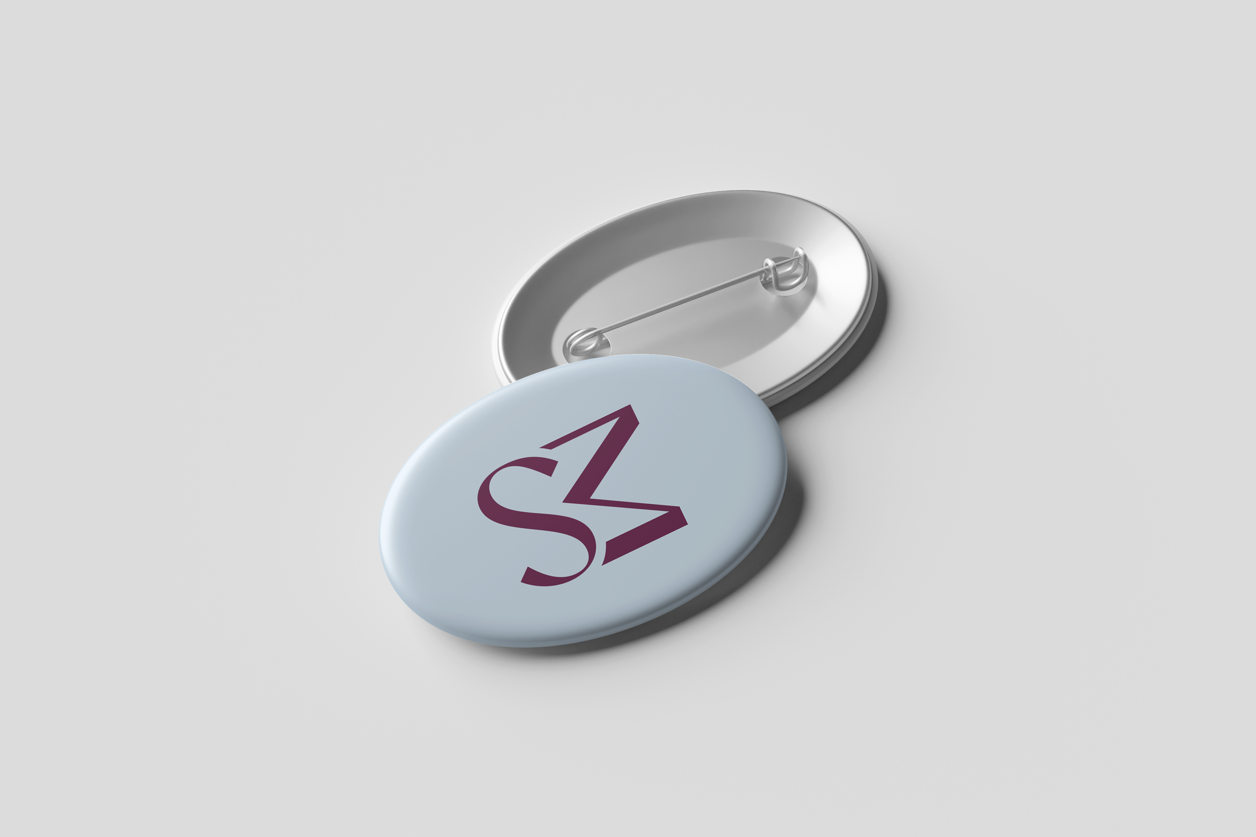 Close-up of a round badge with a safety pin on the back, partially covering a white badge with purple text.