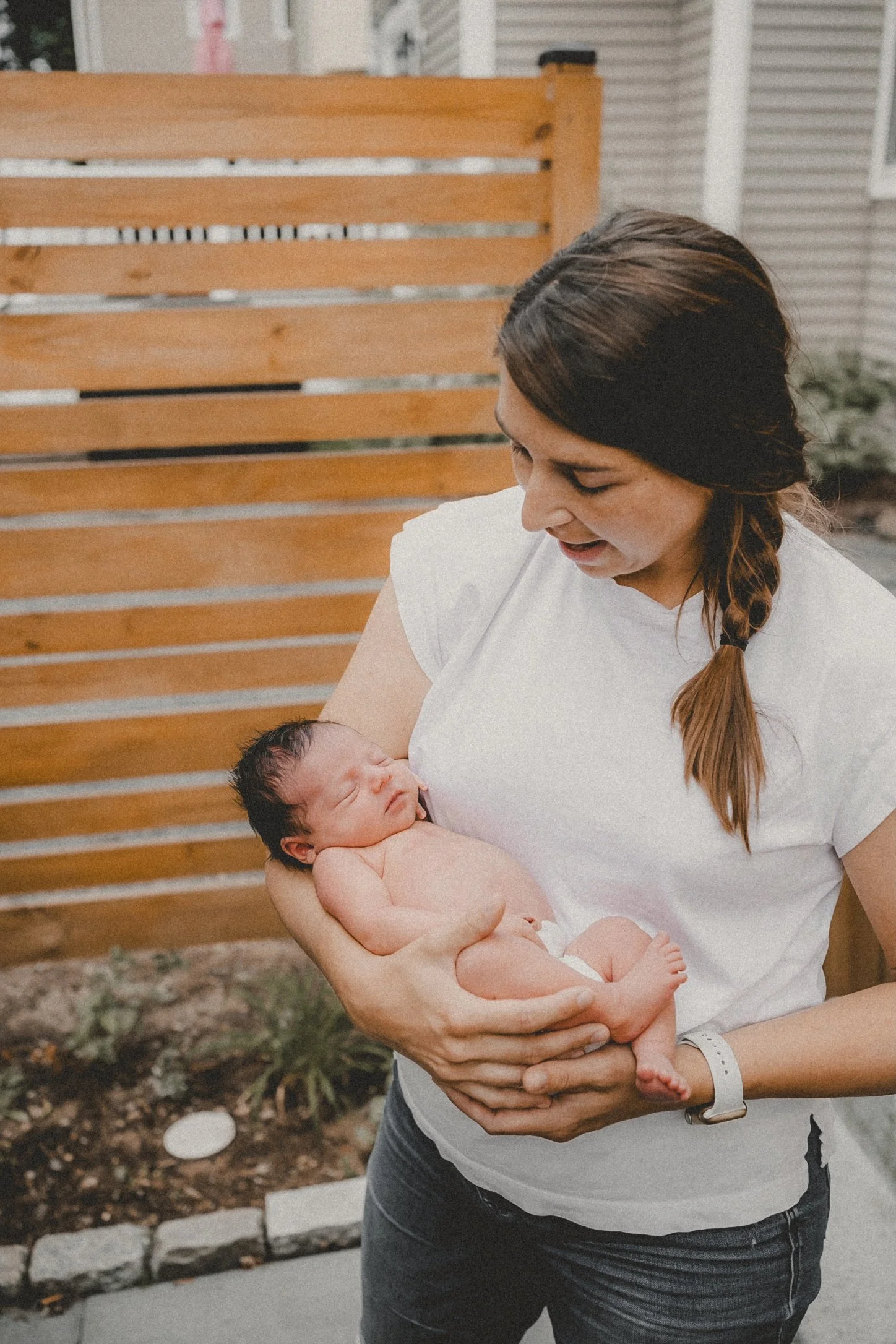 A woman holding a newborn baby outdoors near a wooden fence.