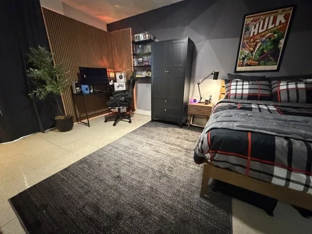 A bedroom with a bed, nightstand, wardrobe, desk, and a framed Hulk comic poster on the wall.