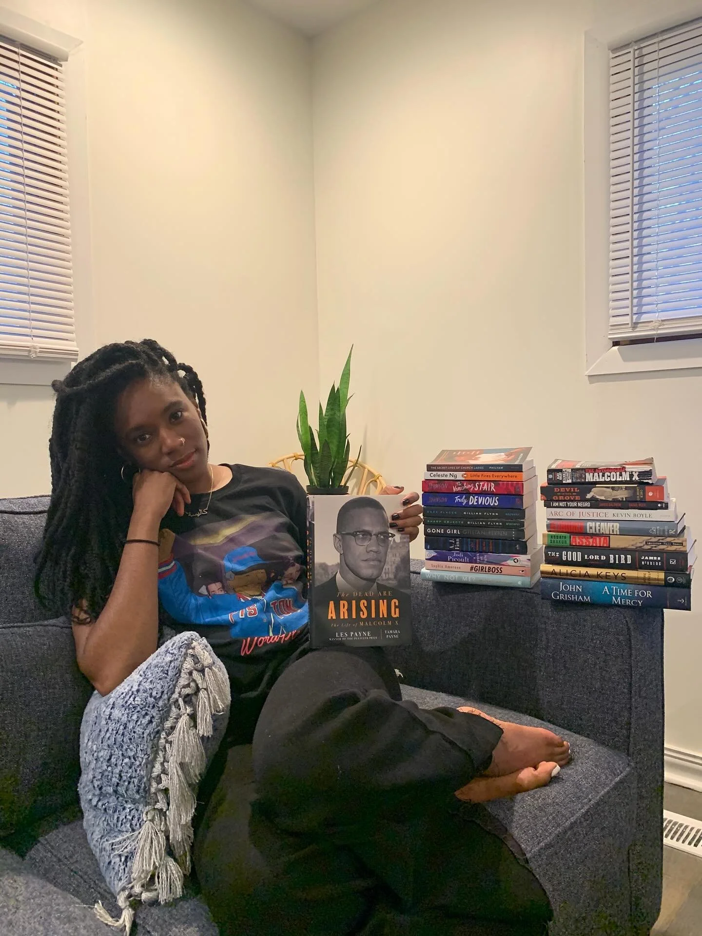 Throwback to December 2020. Just me, a cozy corner, and a stack of (some) banned books. 
I’m holding “The Dead Are Arising”, the Pulitzer Prize–winning biography of Malcolm X by Les Payne and Tamara Payne. In that stack are s