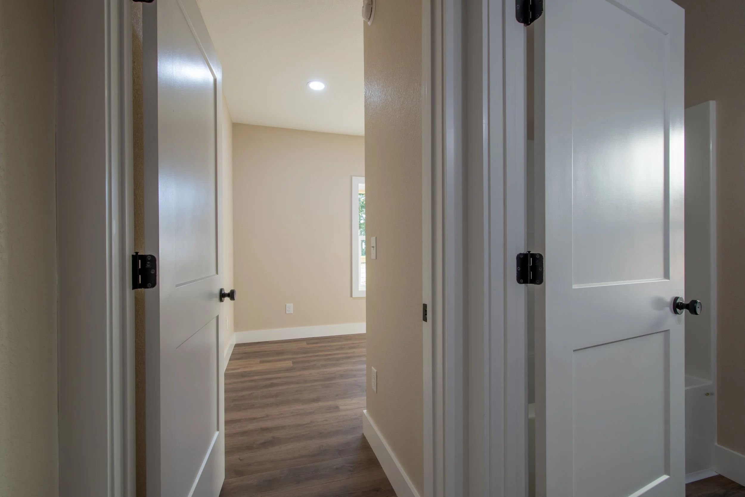 Interior view of a house showing a hallway with two white doors open to closets on the right and a living room with hardwood floors and beige walls in the background.
