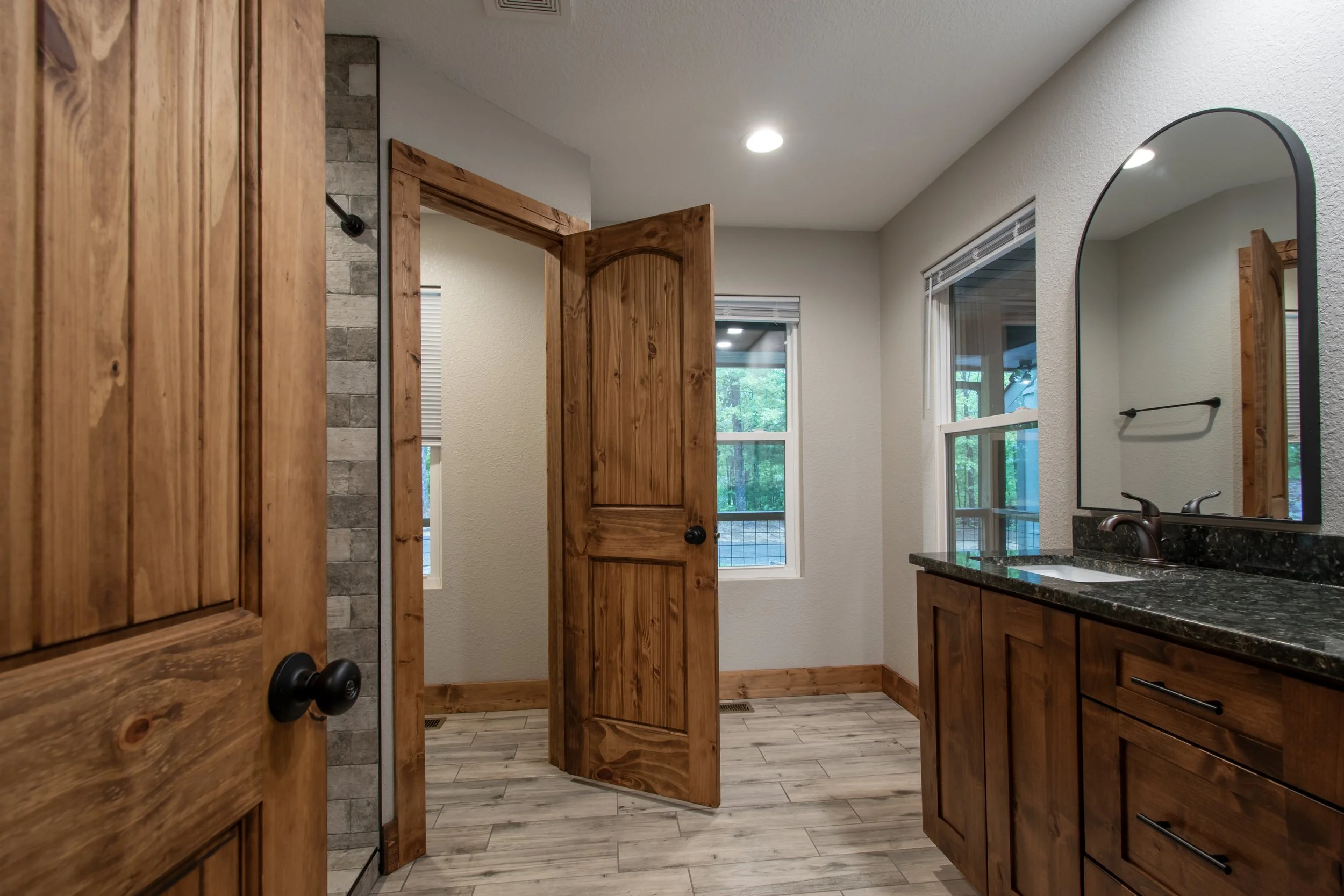 Bathroom with wooden cabinets, a granite countertop, a large mirror, and a window showing trees outside.