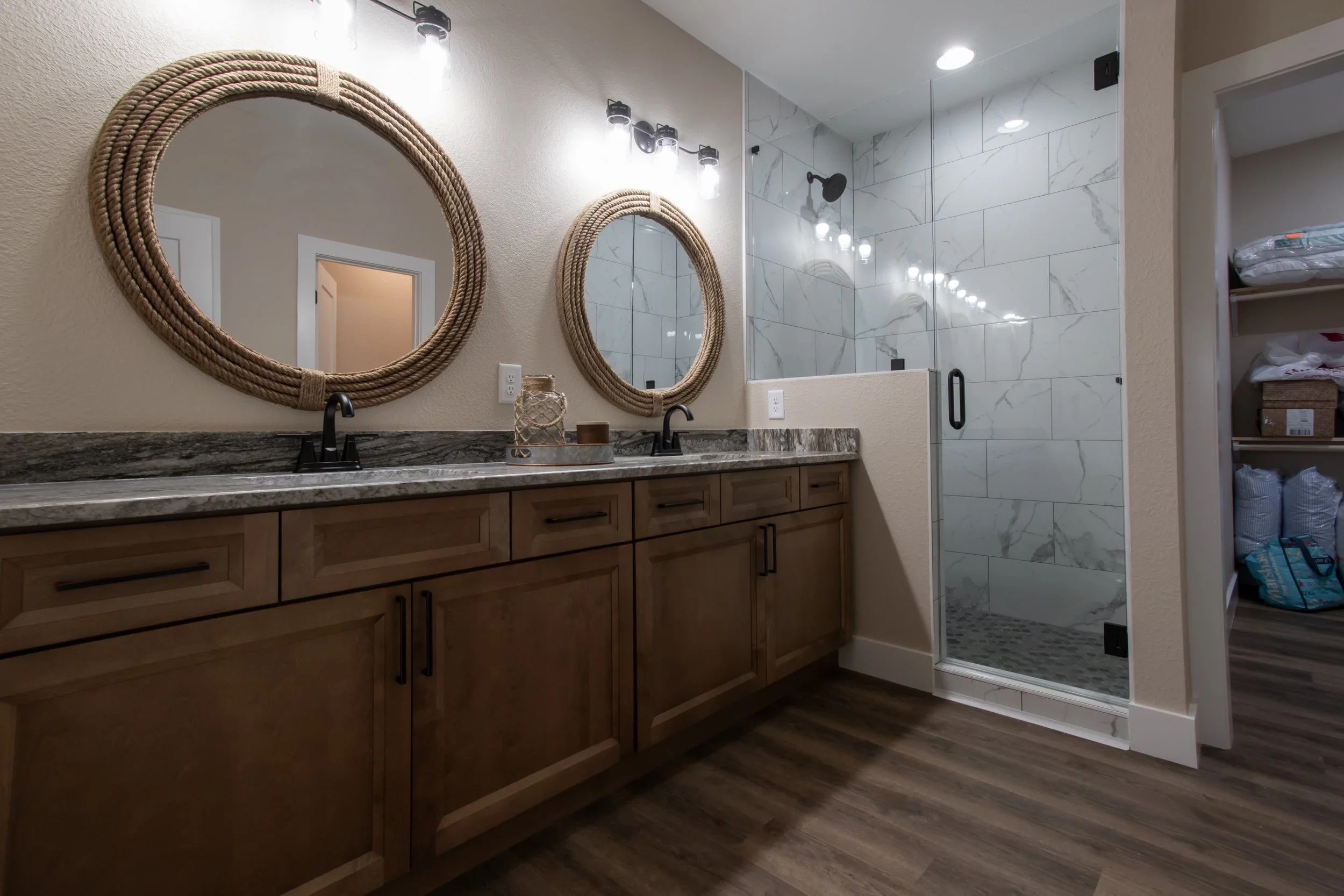 Bathroom with a double vanity, two oval mirrors with rope frames, and a glass-enclosed walk-in shower with marble tiles.