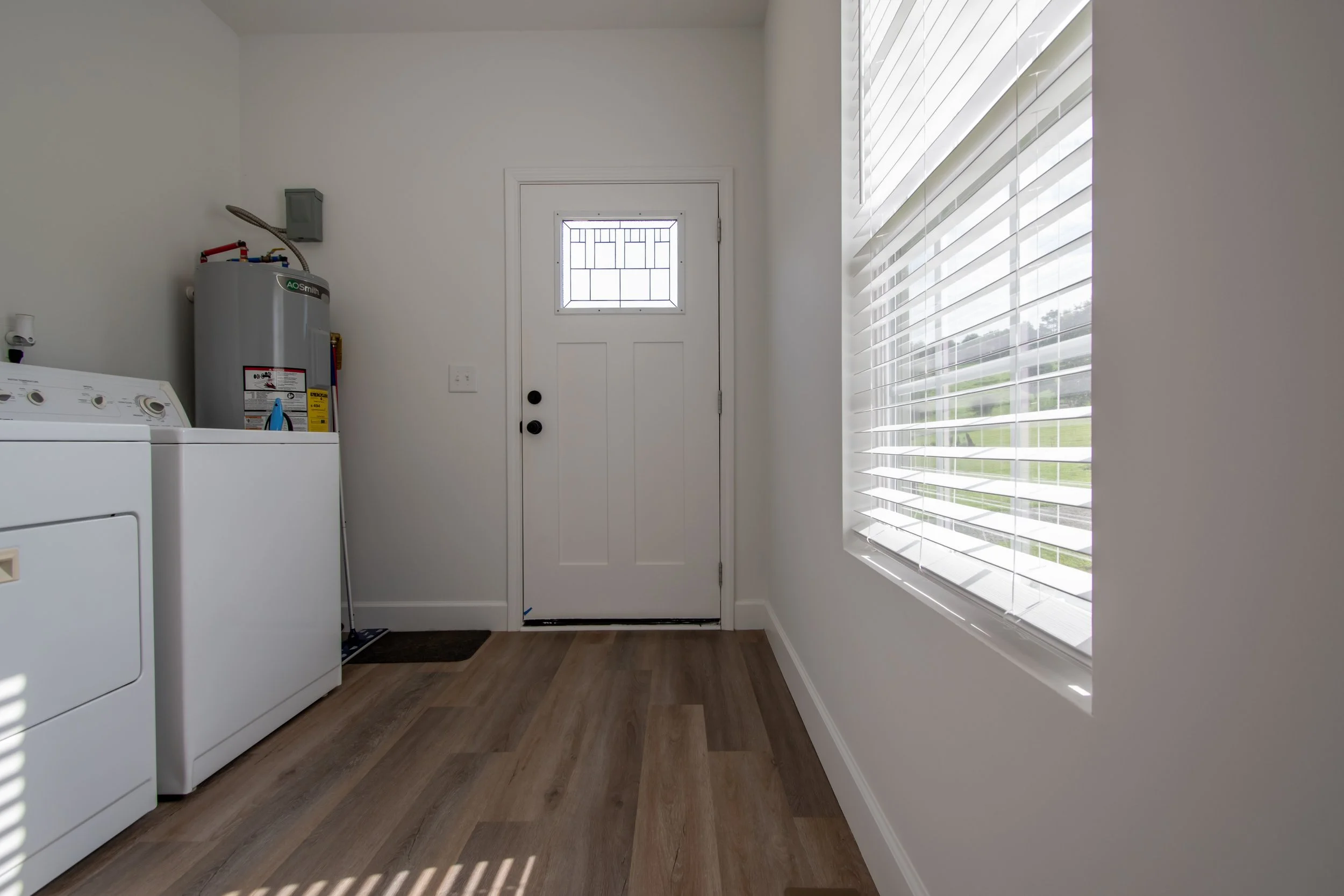 Laundry room with a white washer, water heater, and large window with blinds.