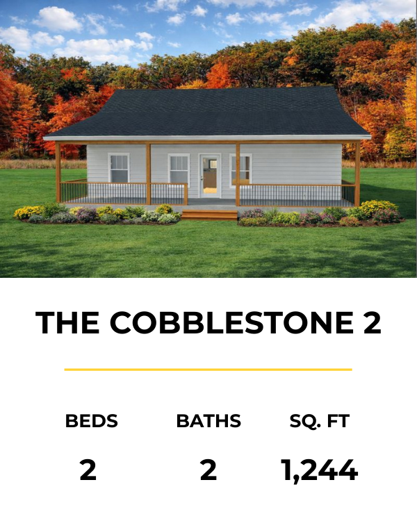 A house with gray siding, a black roof, and a wooden porch, set against a backdrop of fall-colored trees and a green lawn.