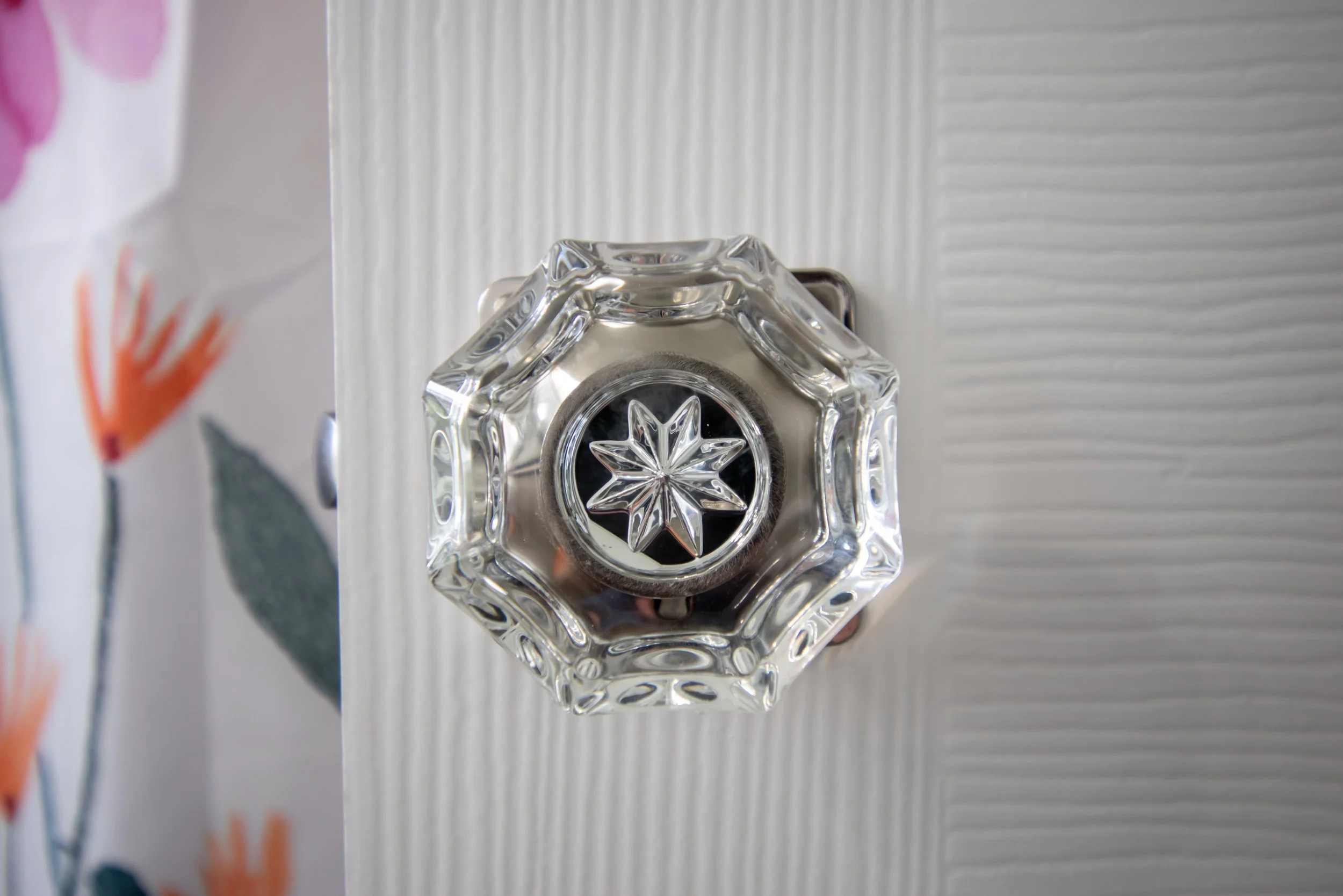 Top view of a decorative glass doorknob with an intricate starburst design on a white textured door.
