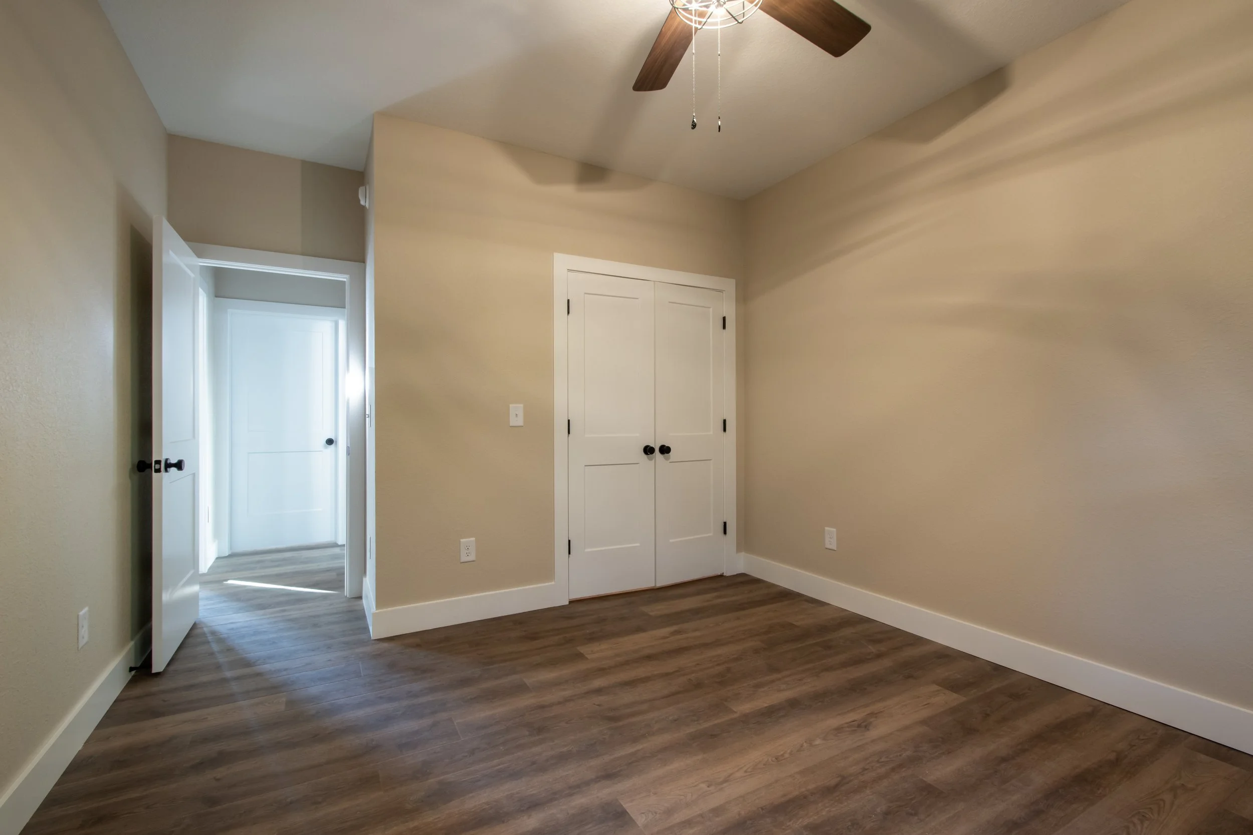 Empty room with wood flooring, beige walls, white doors, and a ceiling fan.