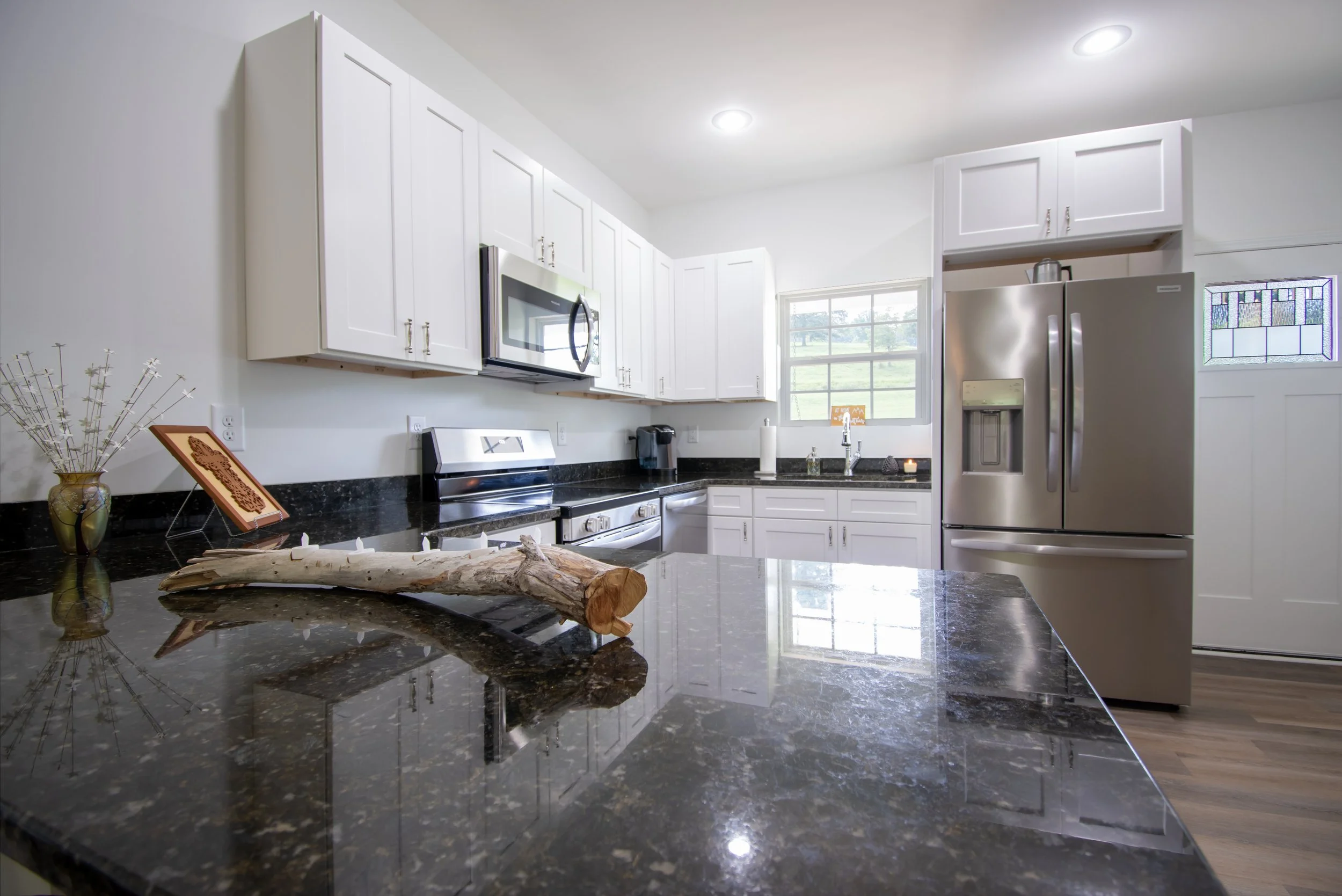 Modern kitchen with white cabinets, black granite countertops, stainless steel appliances, window above sink, and decorative items on the counter.
