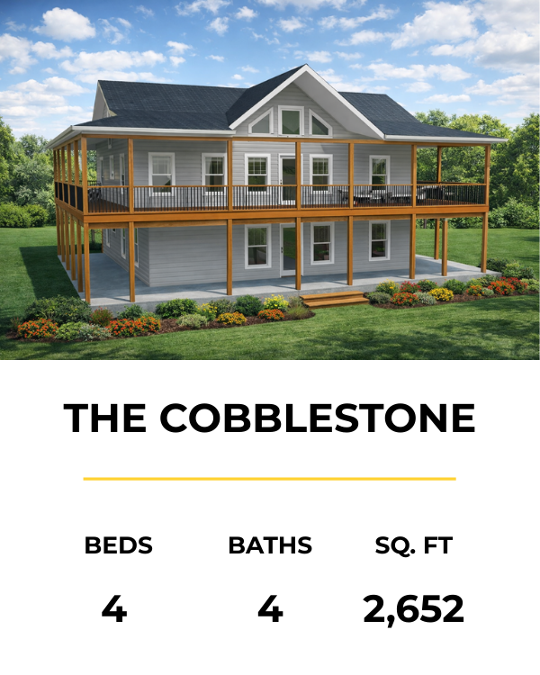 A two-story house with a large wraparound porch, white siding, and a dark roof, set on a grassy lawn with shrubs and flowers in the foreground.