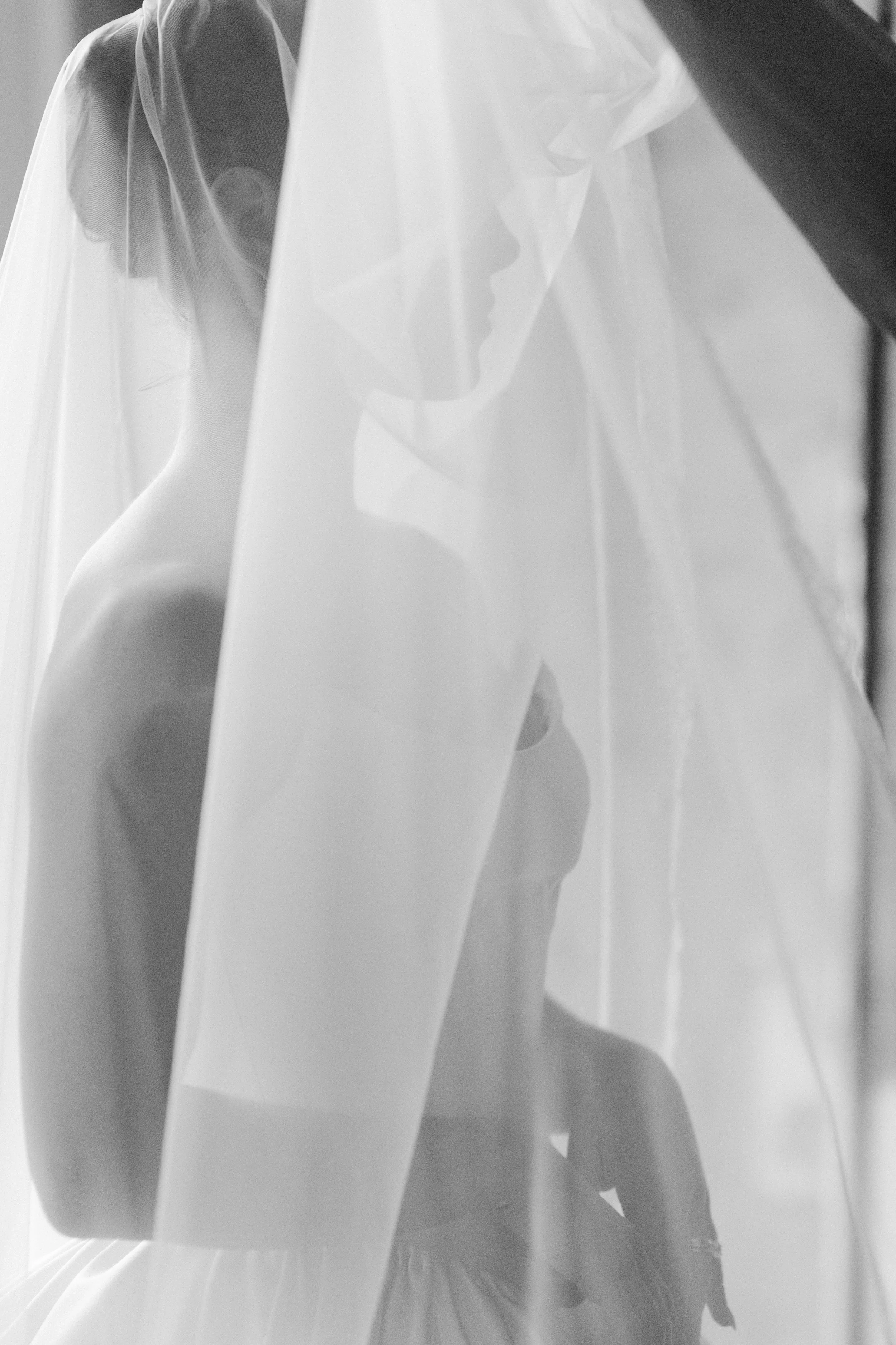A woman wearing a wedding dress and wedding veil, seen through a reflective or semi-transparent surface.