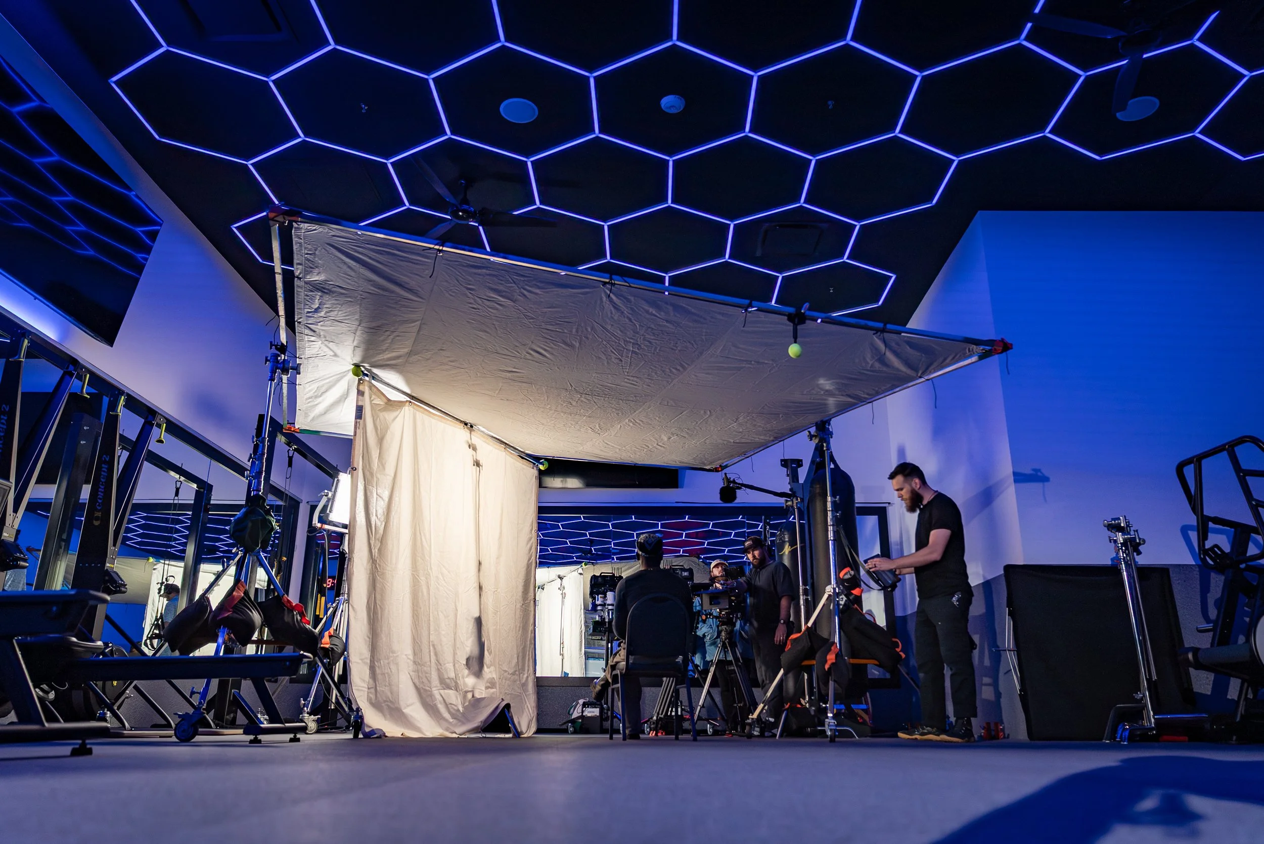 A video crew sets up a large frame with diffusion inside of a futuristic fitness center