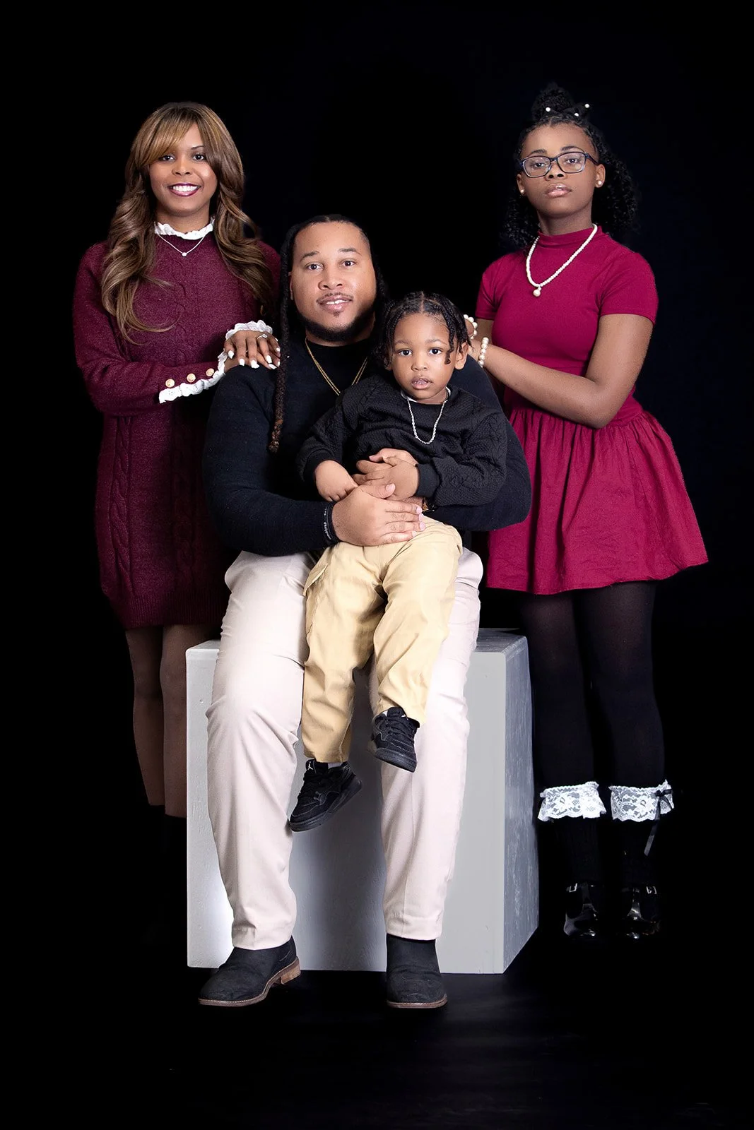 A family of five dressed in black Nike athleticwear posing together in front of a white background with a large black Nike swoosh logo.